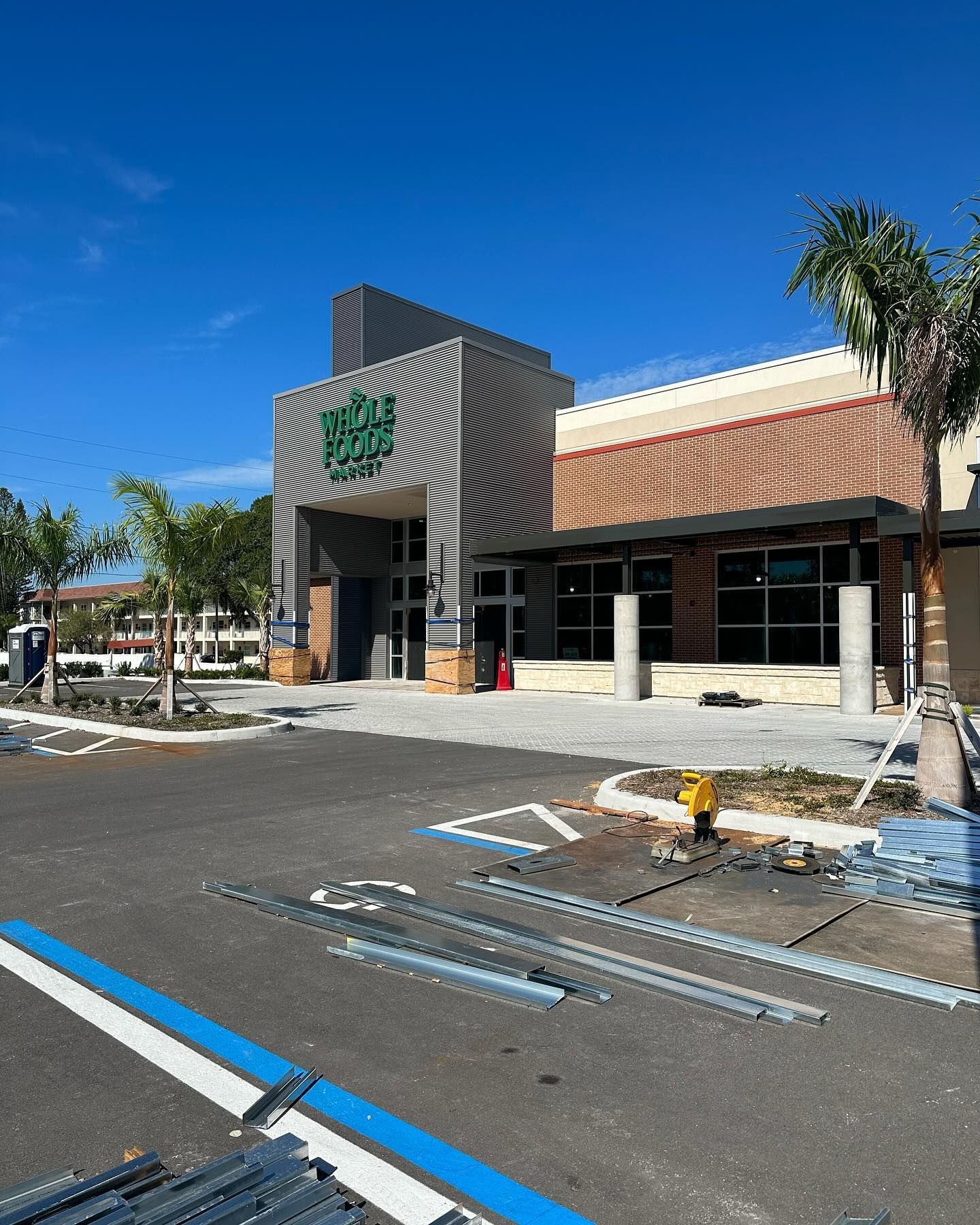 Exterior of a Whole Foods Market building under construction; blue sky, parking area, construction materials.