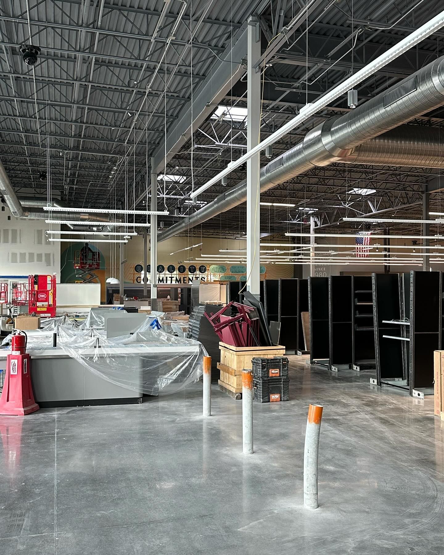 Interior of a store under construction; gray floor, ceiling, and support columns. Cash registers covered, shelving, and equipment.