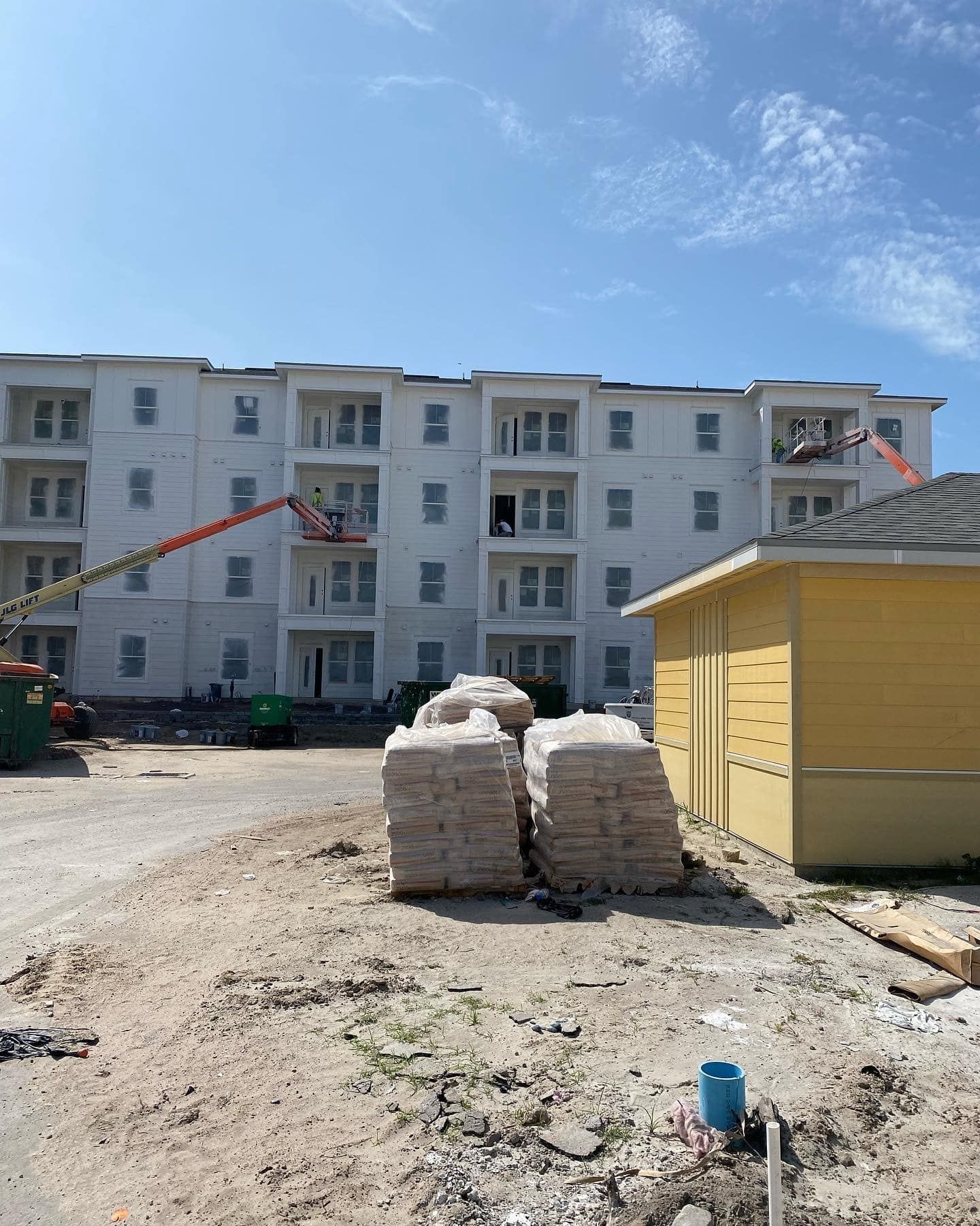 Construction site: multi-story white building, yellow building, bags of materials, blue sky.