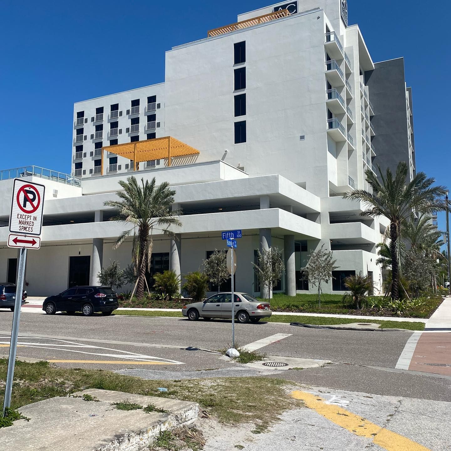 White hotel building with a parking garage, street sign, cars, and palm trees.