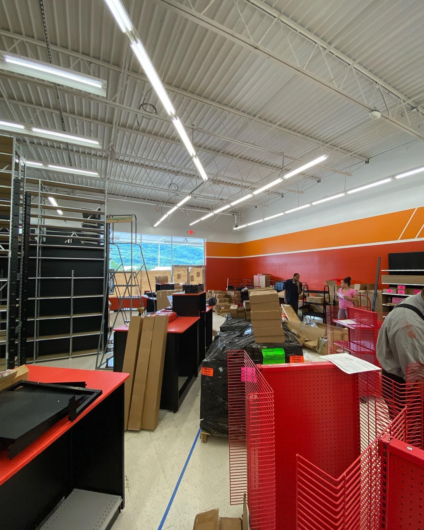 Interior of store being set up: shelving, boxes, workers in orange and white space.