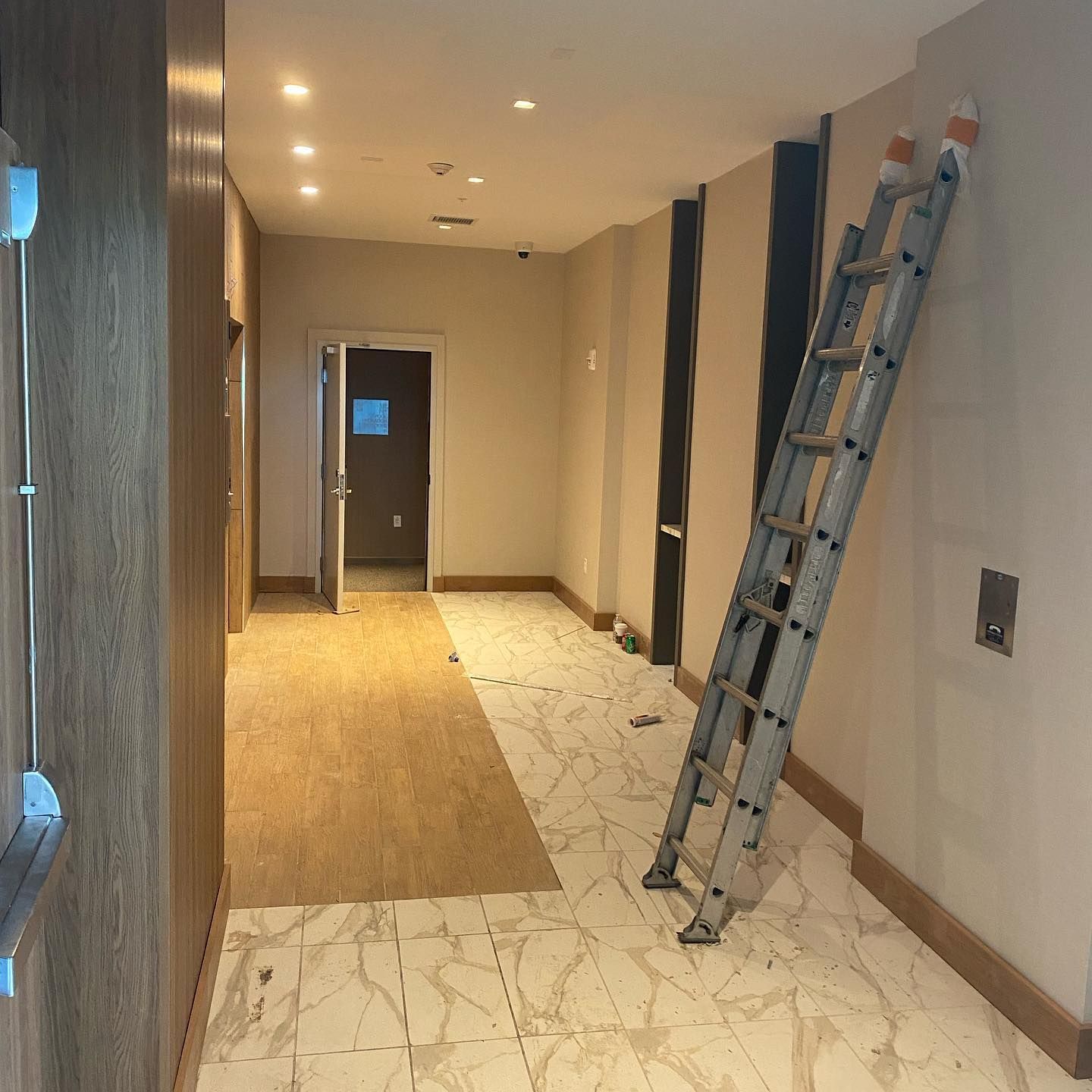 A narrow hallway under construction with a tall ladder propped against the wall and unfinished flooring.