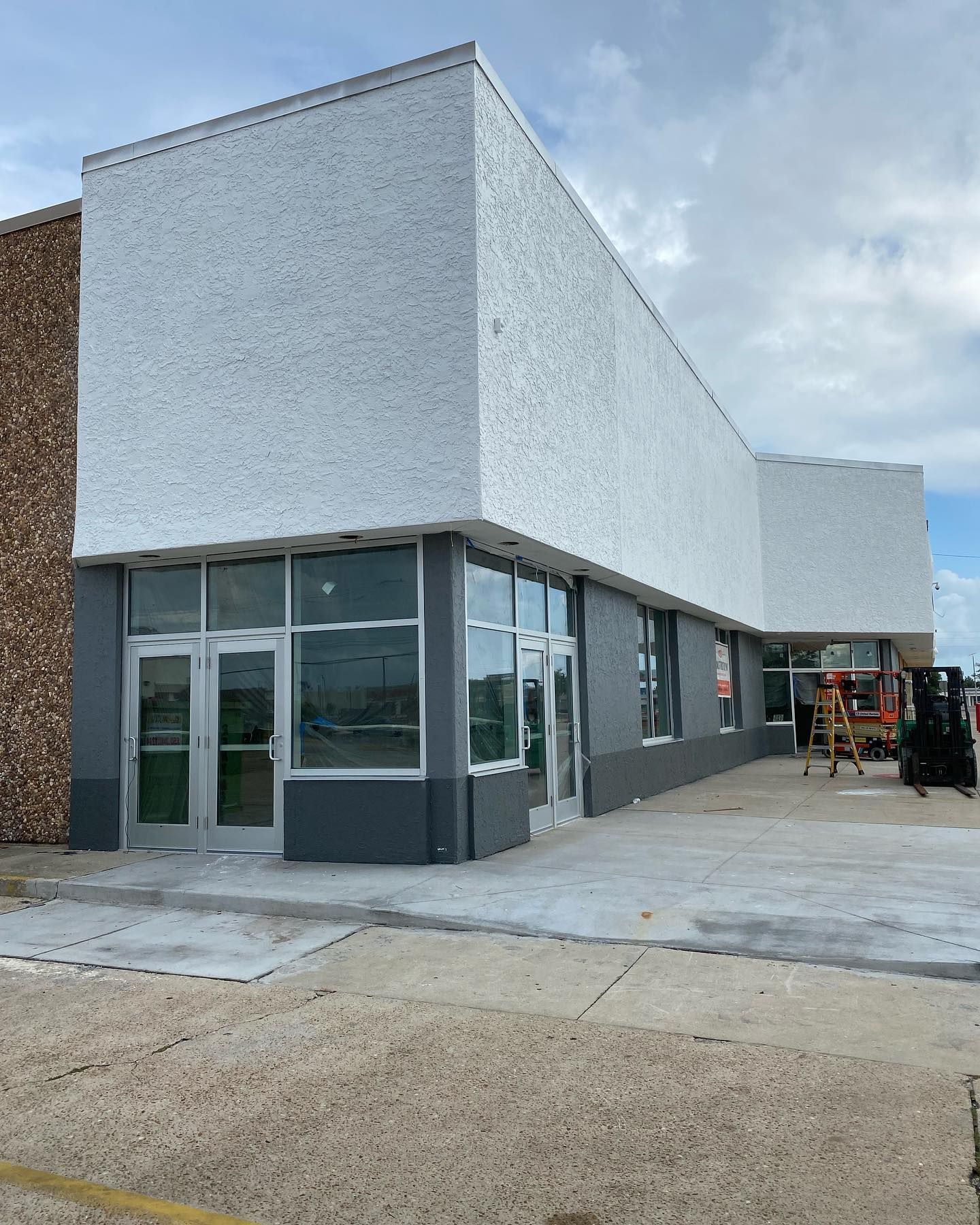 Exterior of a commercial building with gray and white stucco. Glass windows and doors are visible.