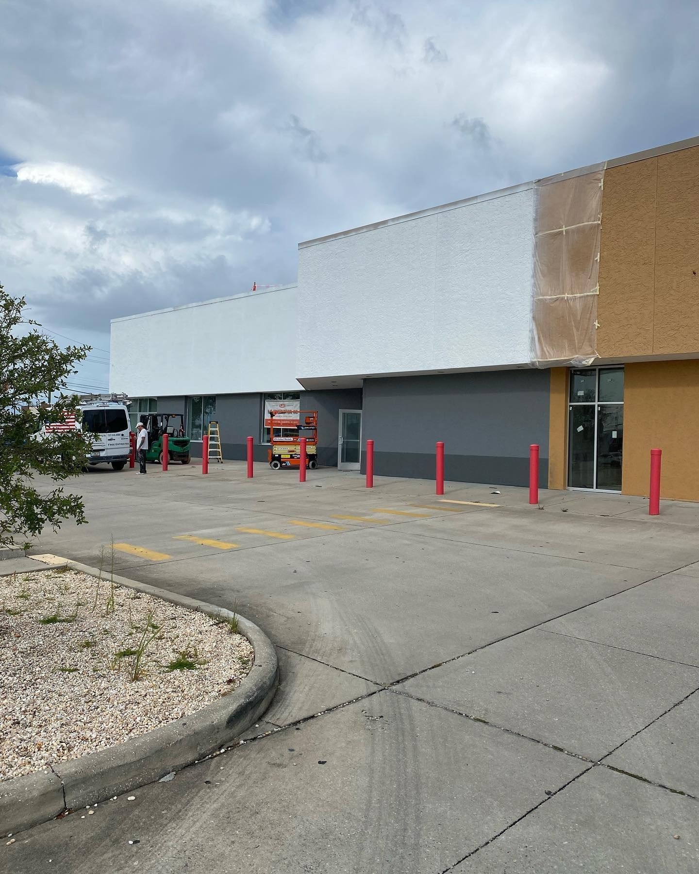 Exterior of a building being painted. Gray, white, and tan sections. Parking lot in front.