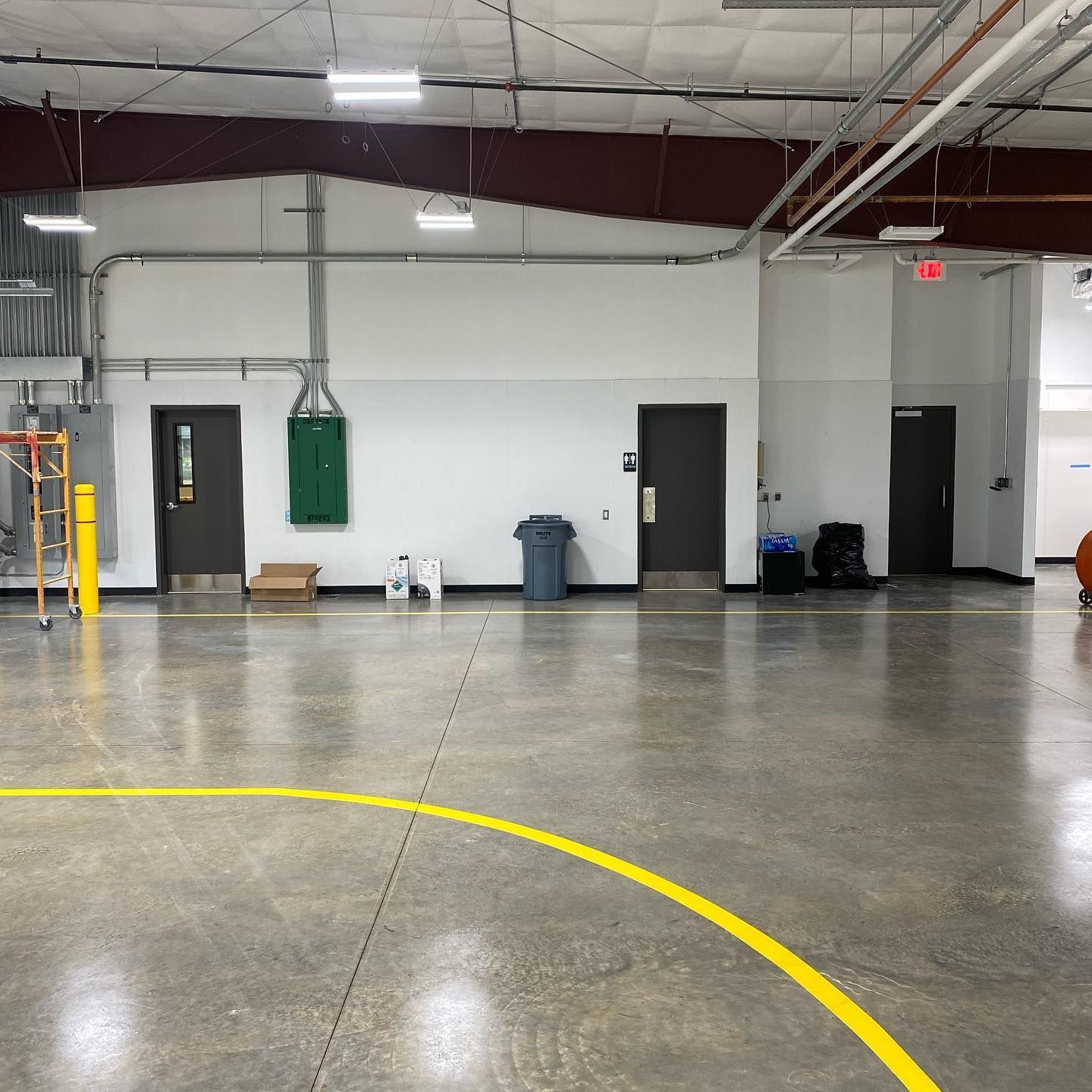 An empty indoor gym with doors, trash can, and a basketball court line.
