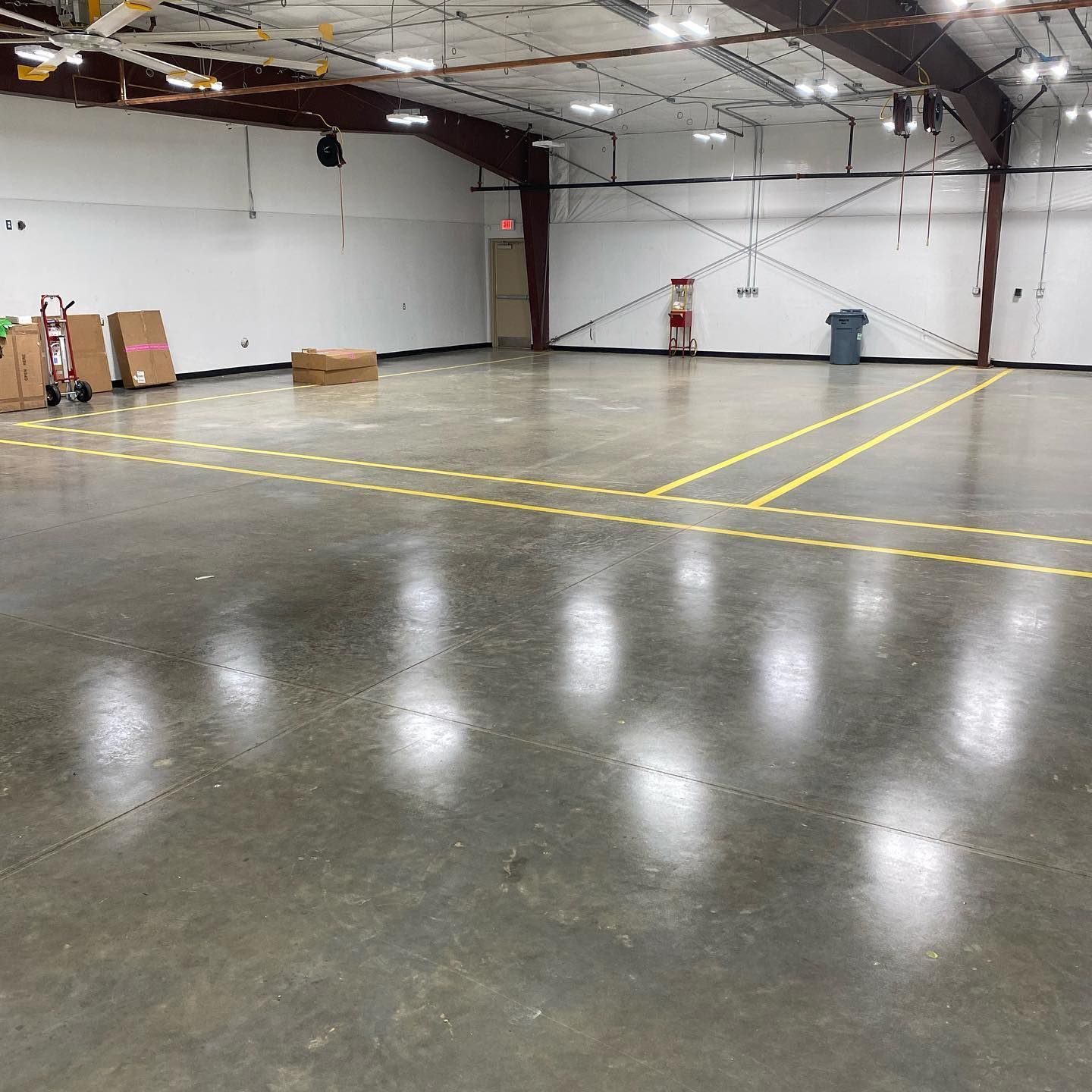 Empty warehouse with concrete floor, yellow lines, boxes, and overhead lights.