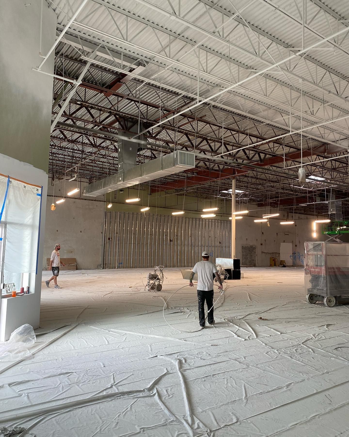 Construction site: Workers in a large, open space. White flooring, exposed ceiling beams.