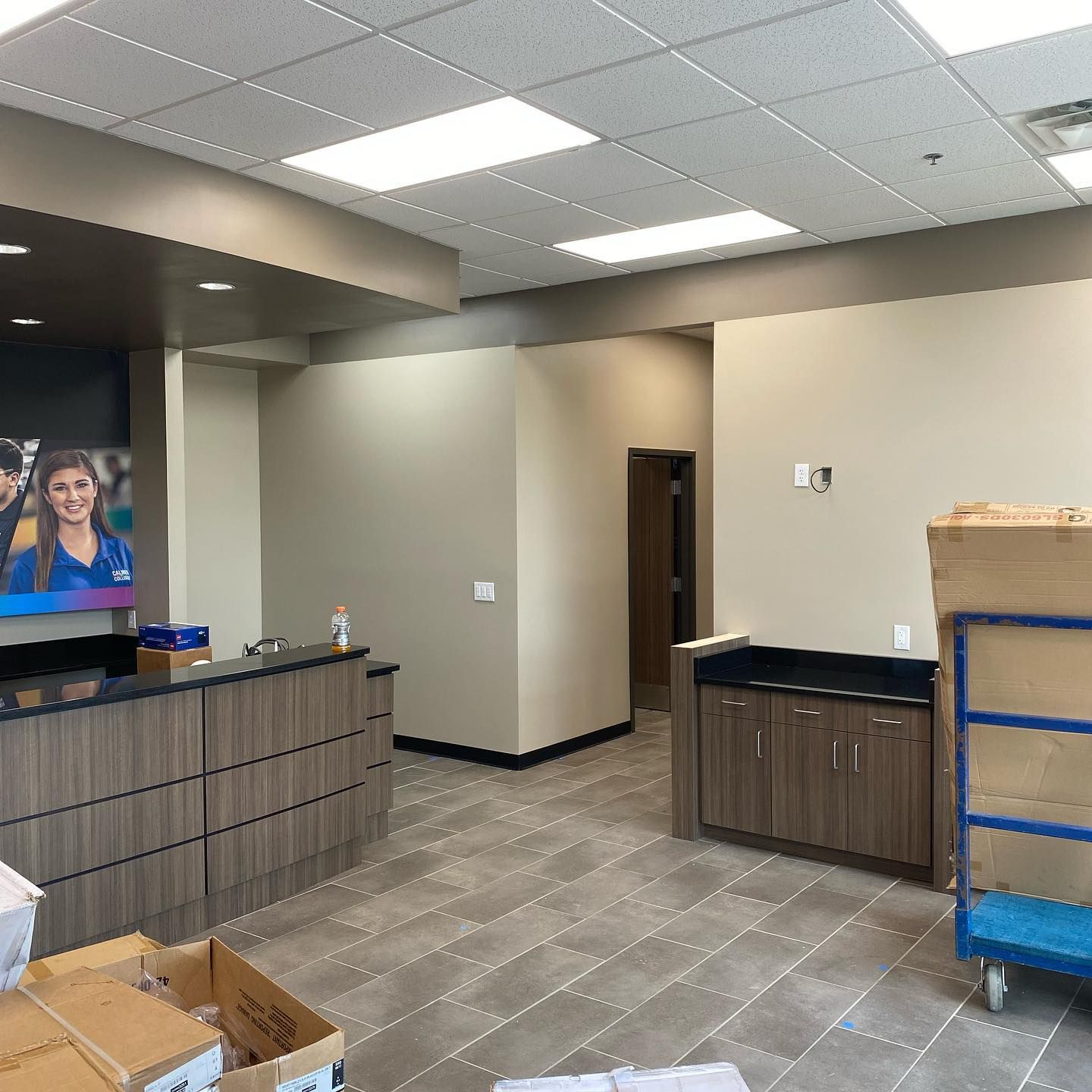 Interior of an office reception area, with a front desk, tiled floor, tan walls, and built-in cabinetry.
