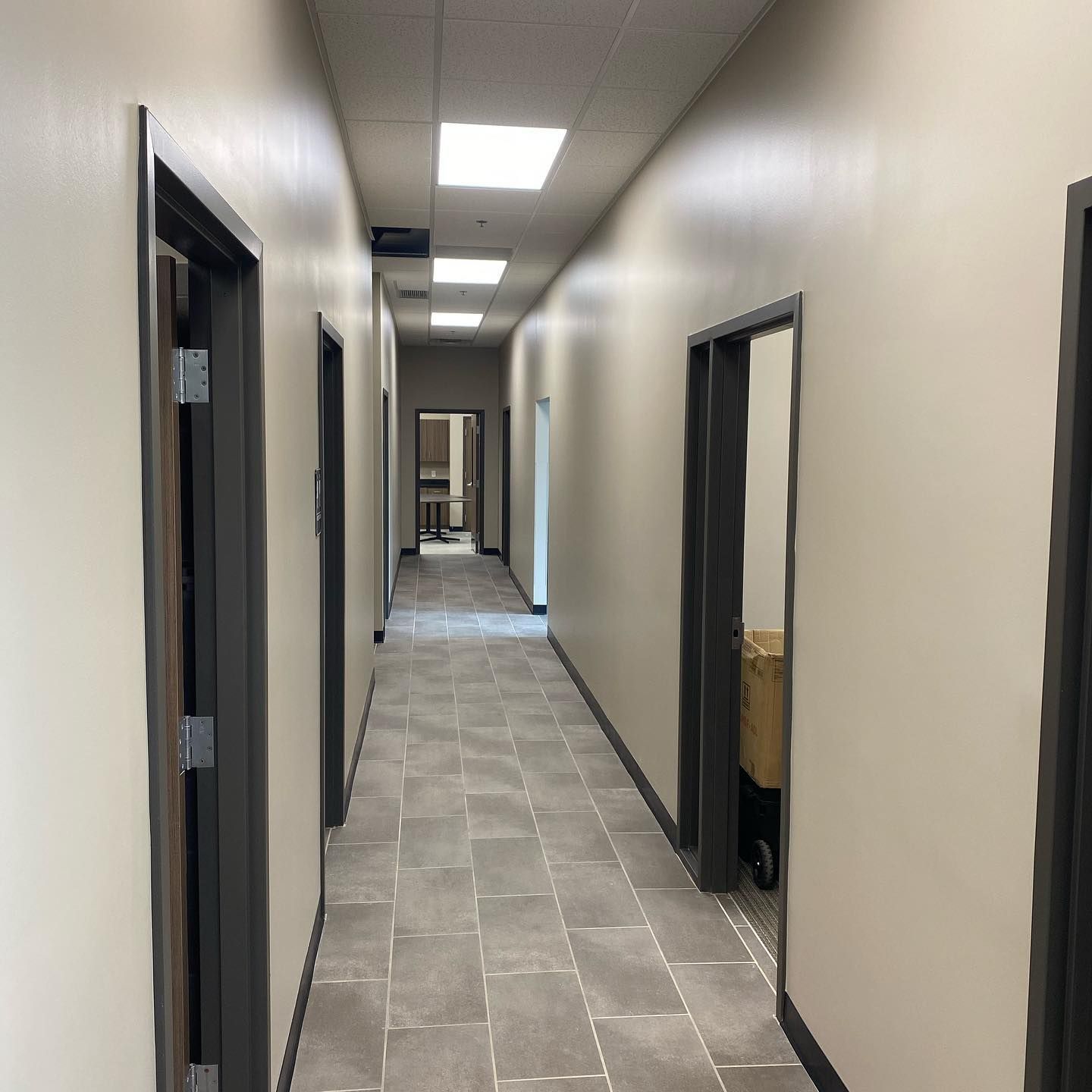 Hallway with gray tile flooring, beige walls, and dark gray door frames.