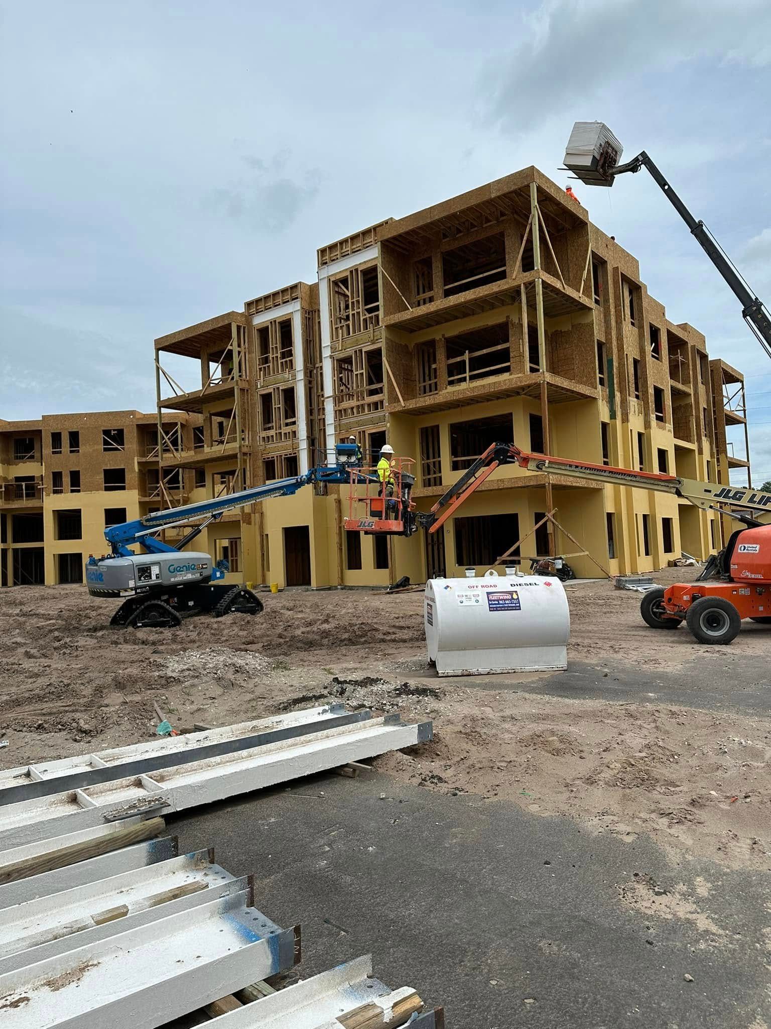 Construction site: multi-story building under construction, wooden frame, aerial lifts, cloudy sky.