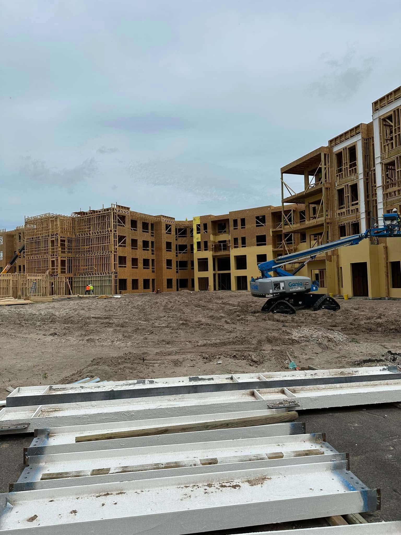 Construction site: wooden apartment buildings under construction, dirt ground, cloudy sky.