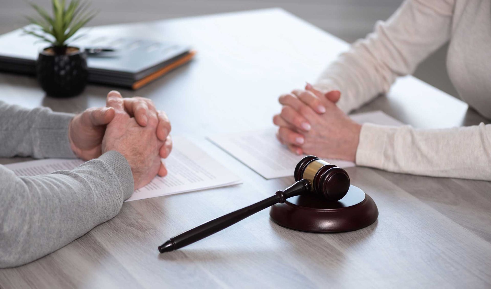 Two people sitting across from each other at a table with a judge's gavel and legal documents Two people sitting across from each other at a table with a judge's gavel and legal documents