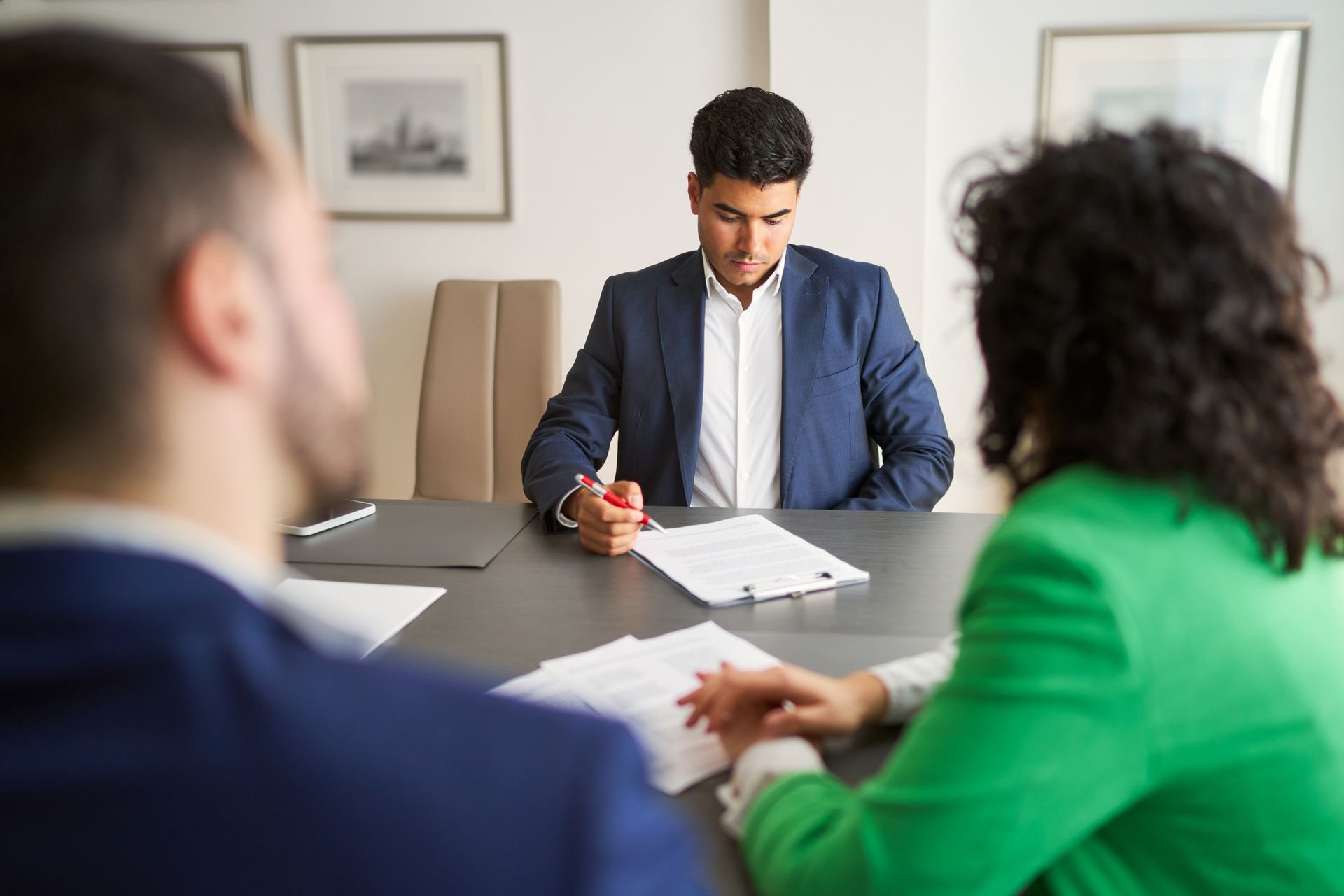 Three people are sitting at a table with papers in front of them. Three people are sitting at a table with papers in front of them.