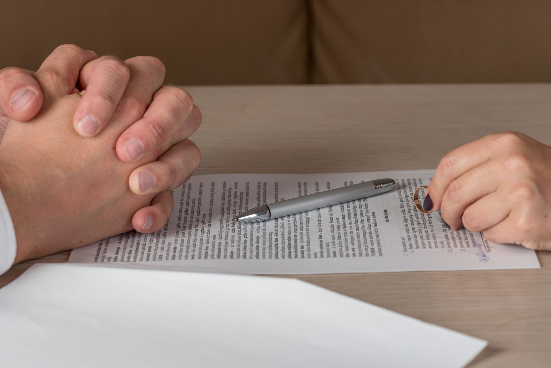 Hands over divorce papers with pen and wedding ring during legal separation process.
