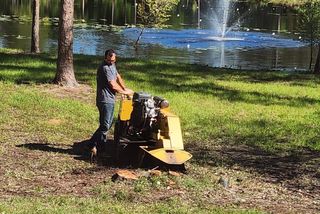 A man is using a stump grinder to remove a tree stump in a park.