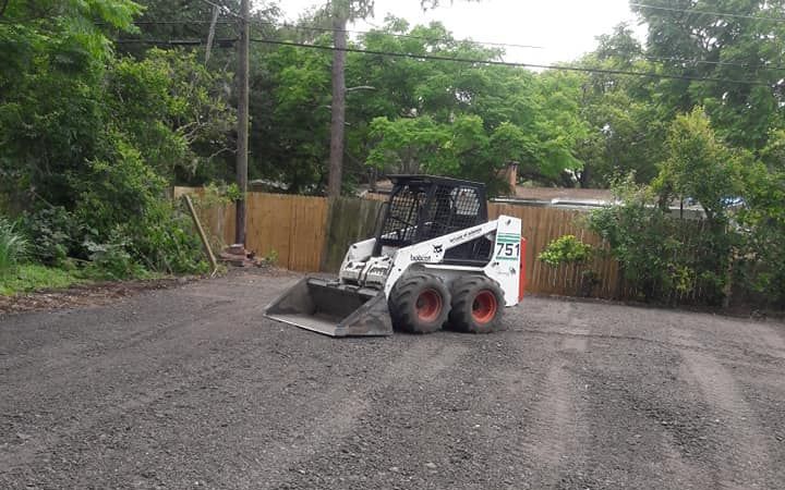 A bobcat is driving down a gravel road in a parking lot.