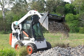 A bobcat is loading dirt into a bucket in a field.