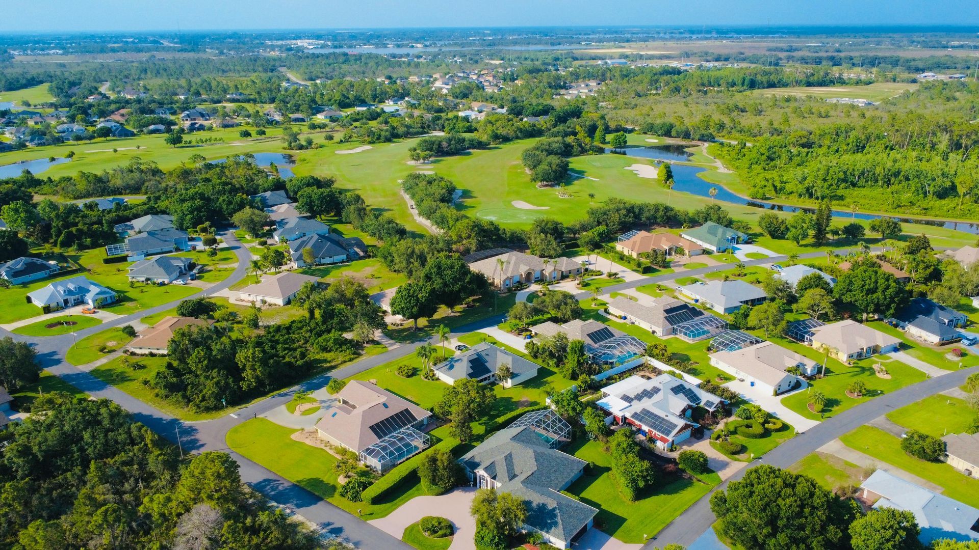 Aerial view of a suburban neighborhood with houses, roads, and green trees under a clear sky