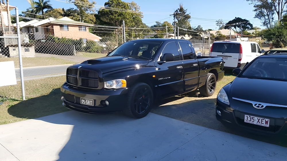 A Black Truck Is Parked In A Driveway Next To A Gray Car — Mudgeeraba Auto Electrical & Mechanical In Mudgeeraba, QLD