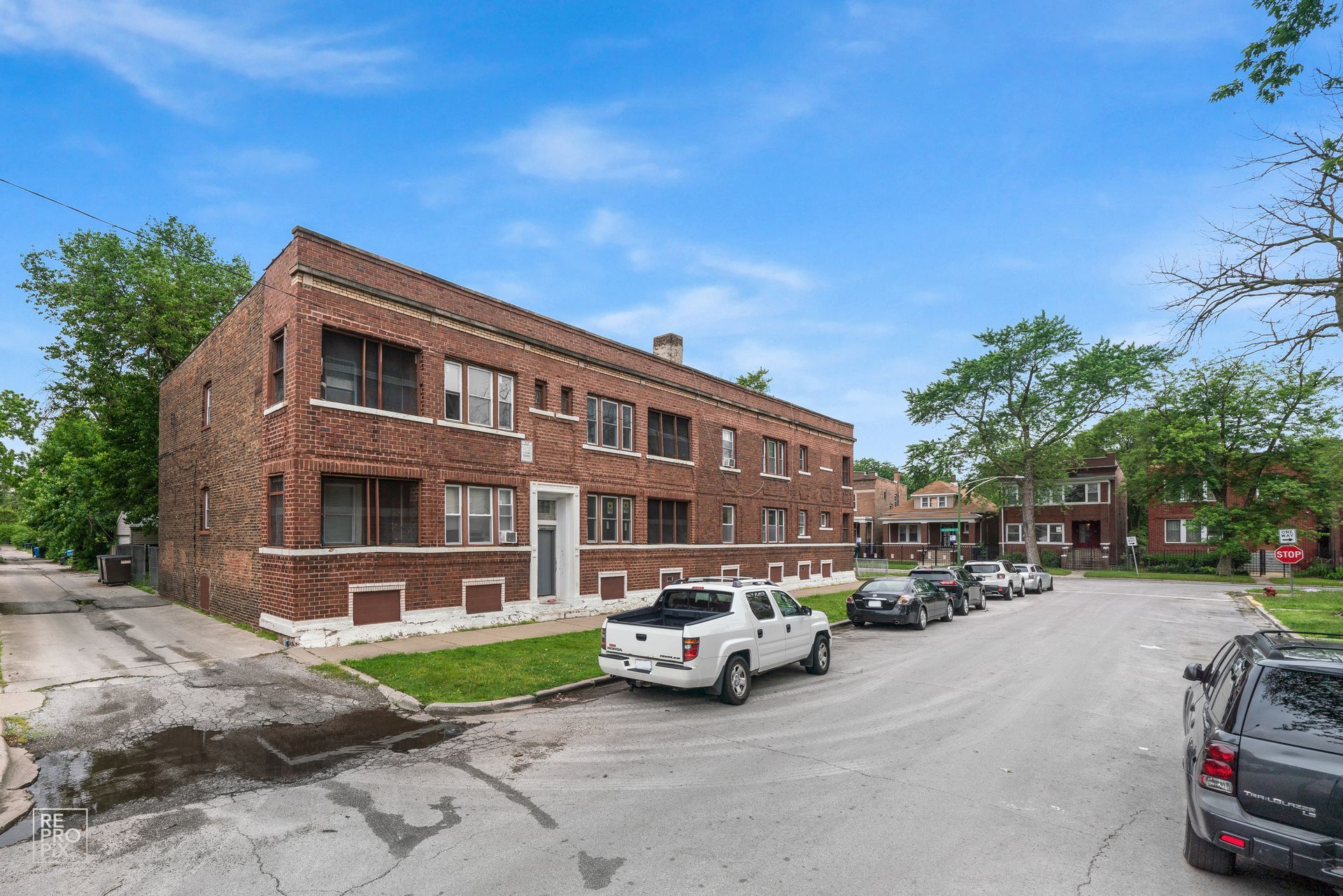 Two-story brick apartment building on a residential street; parked cars, blue sky.