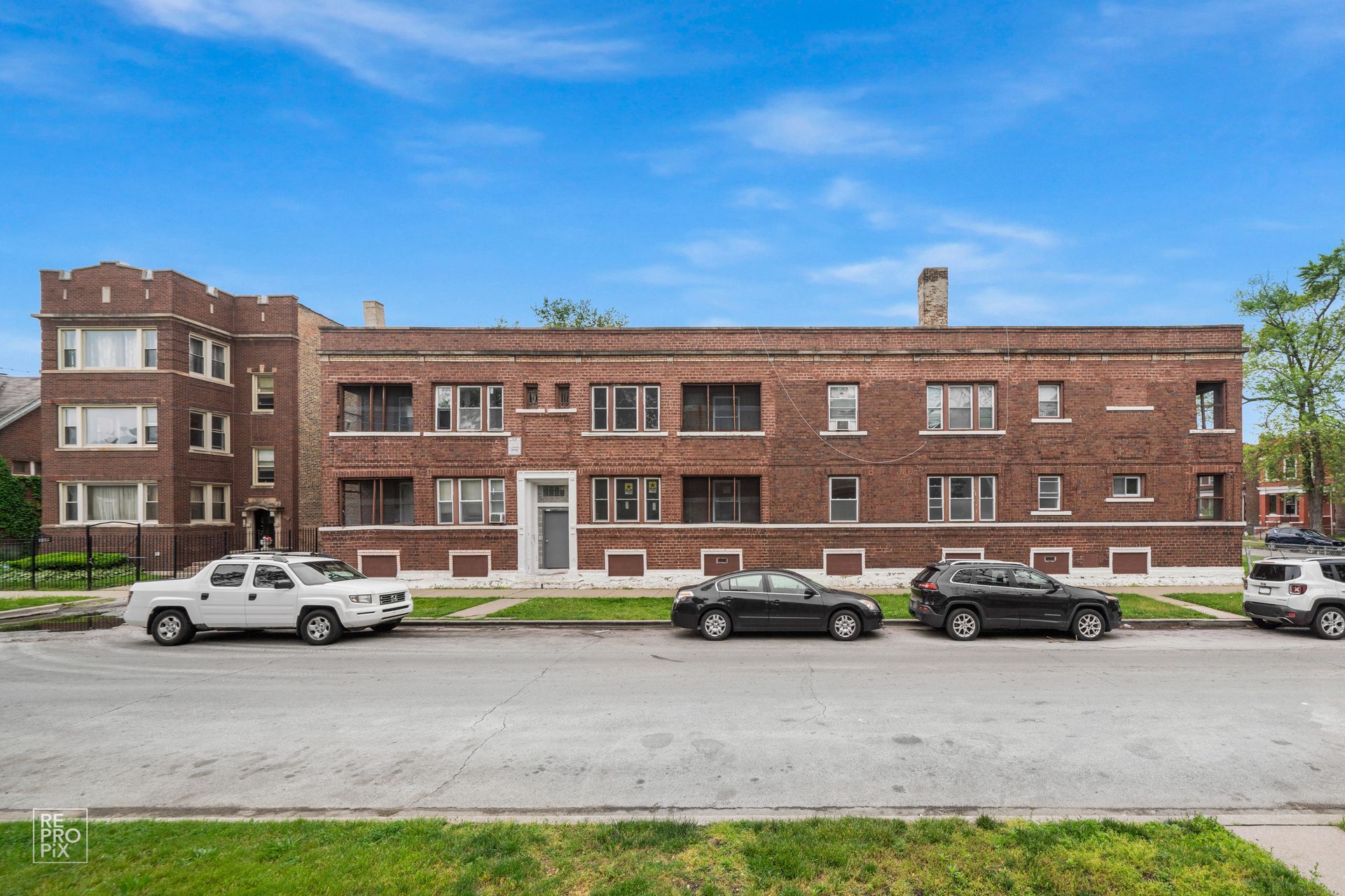 Red brick apartment building with parked cars on a sunny street.