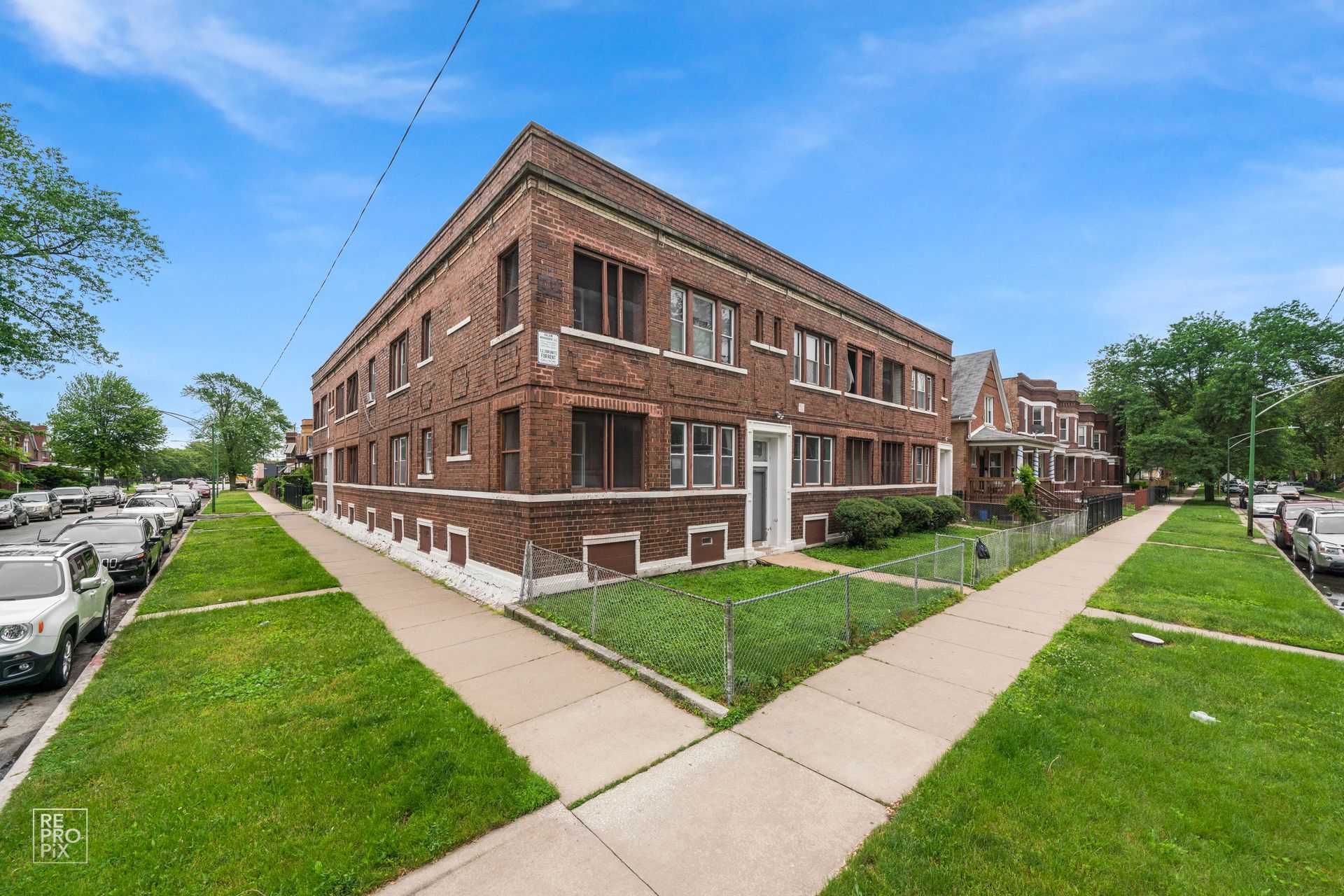 Brick apartment building on a sunny day with green lawn and sidewalk.