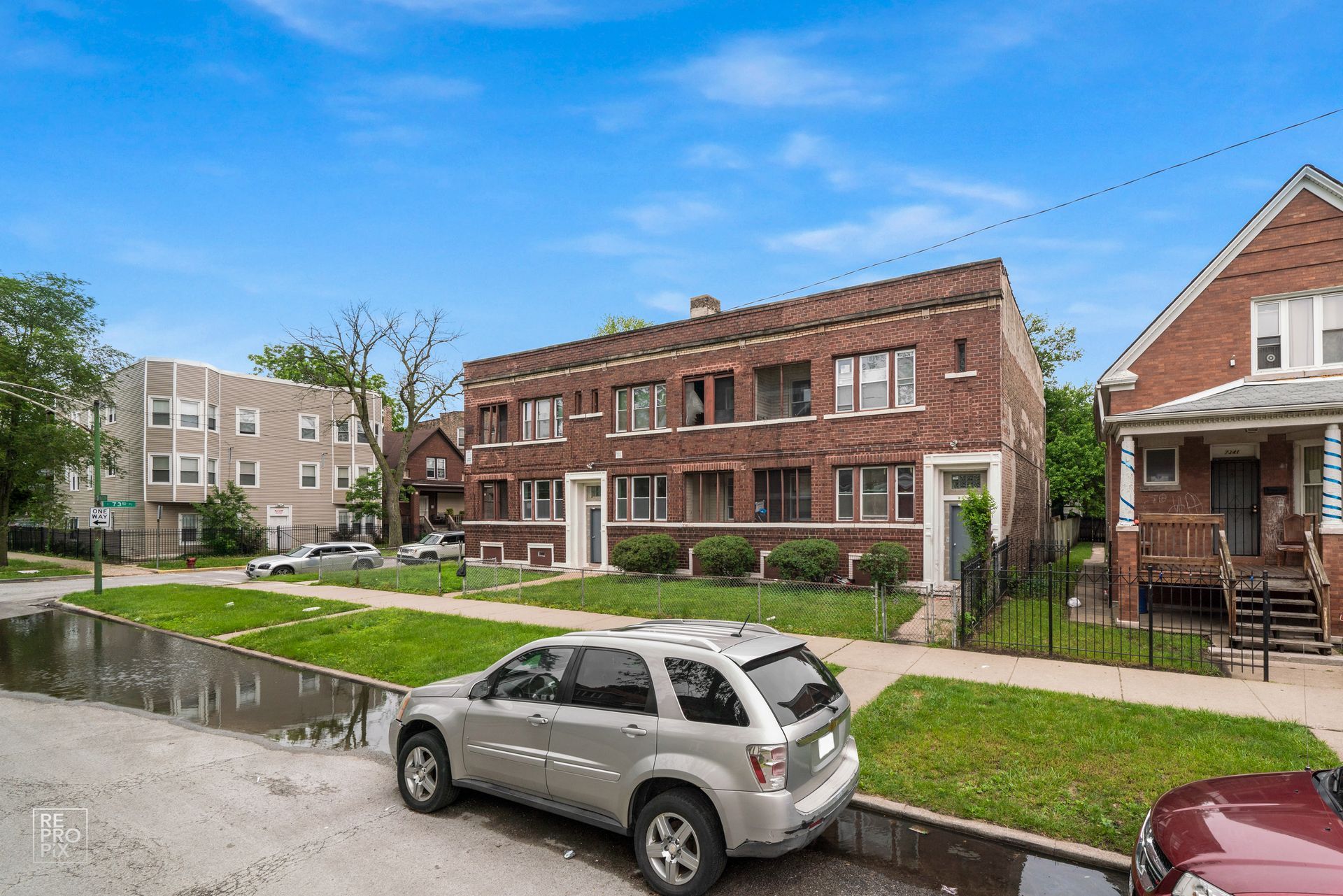 Brick multi-unit building with cars parked on the street on a sunny day.