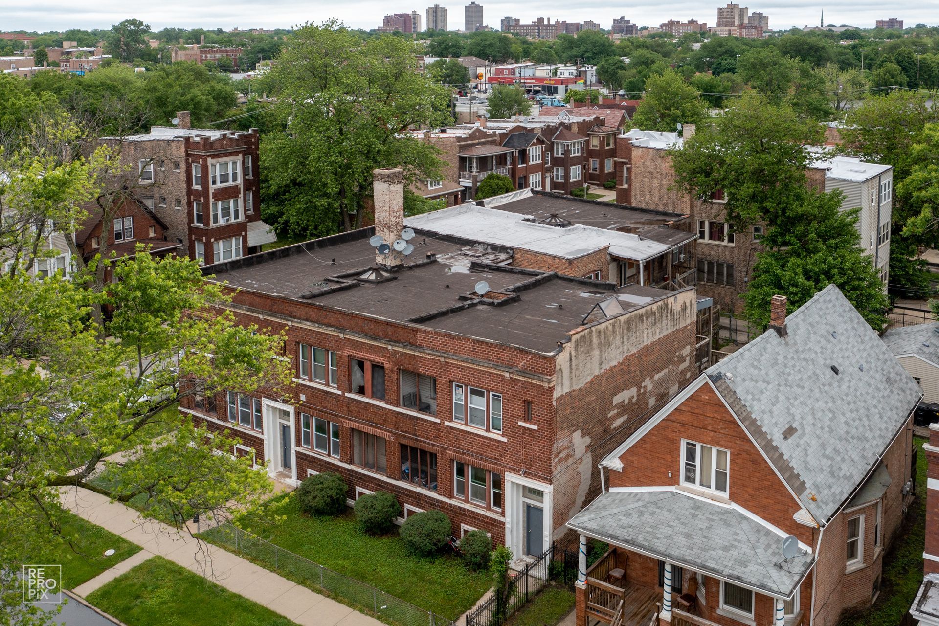 Aerial view of brick apartment buildings and houses with green trees and a city skyline.