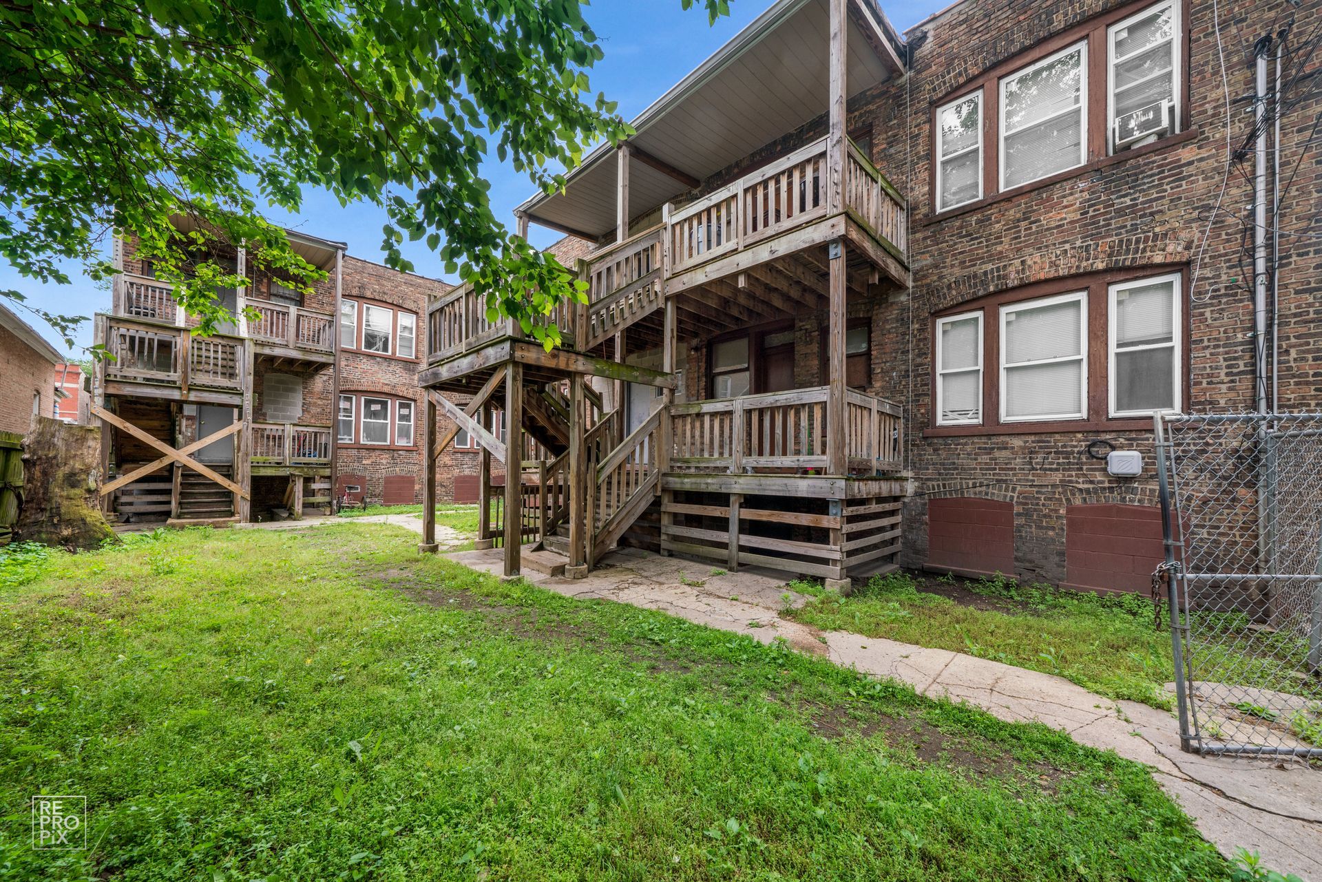 Backyard view of brick apartment building with wooden decks and stairs, green lawn.