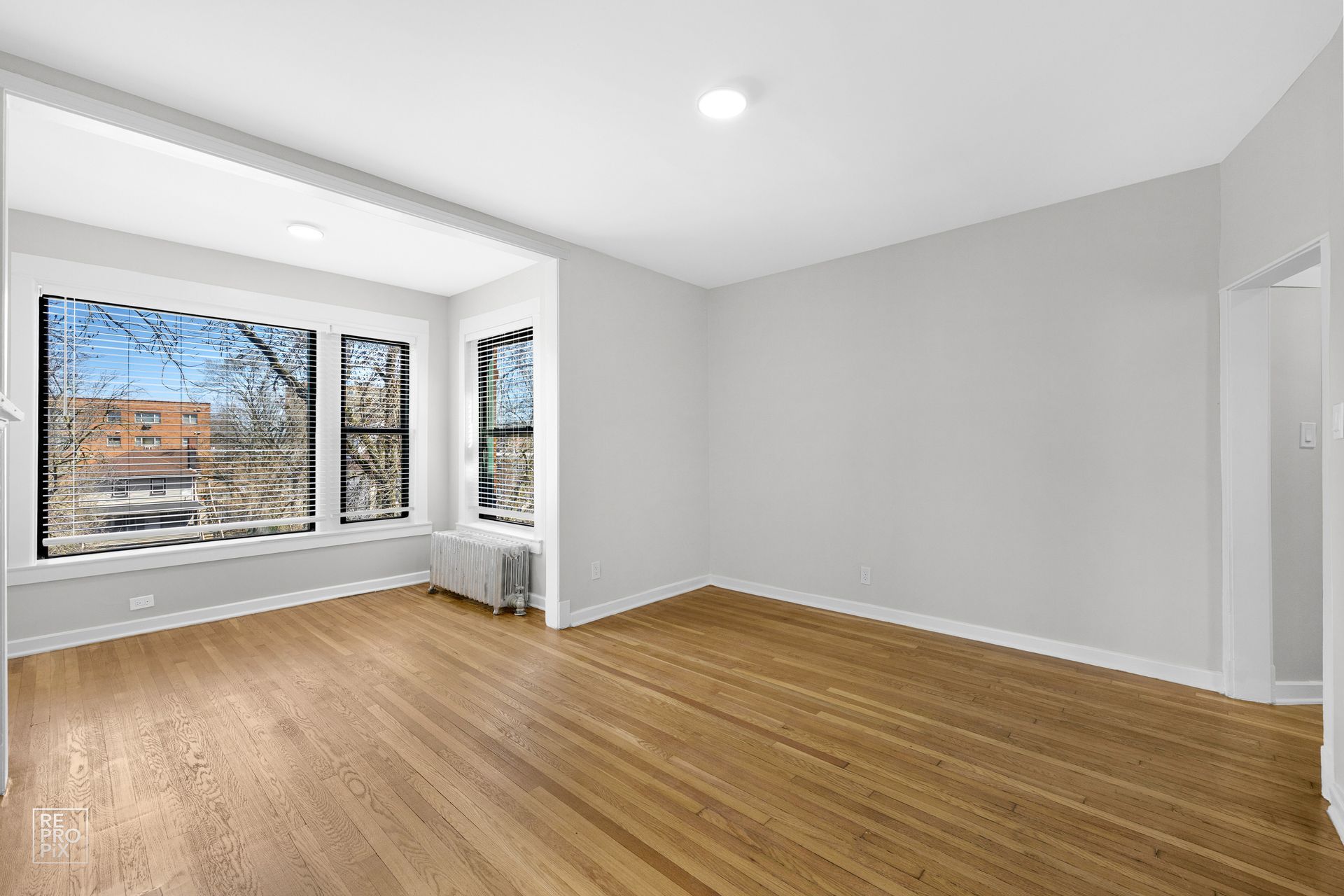 Empty room with wood floors and large bay window overlooking a street.