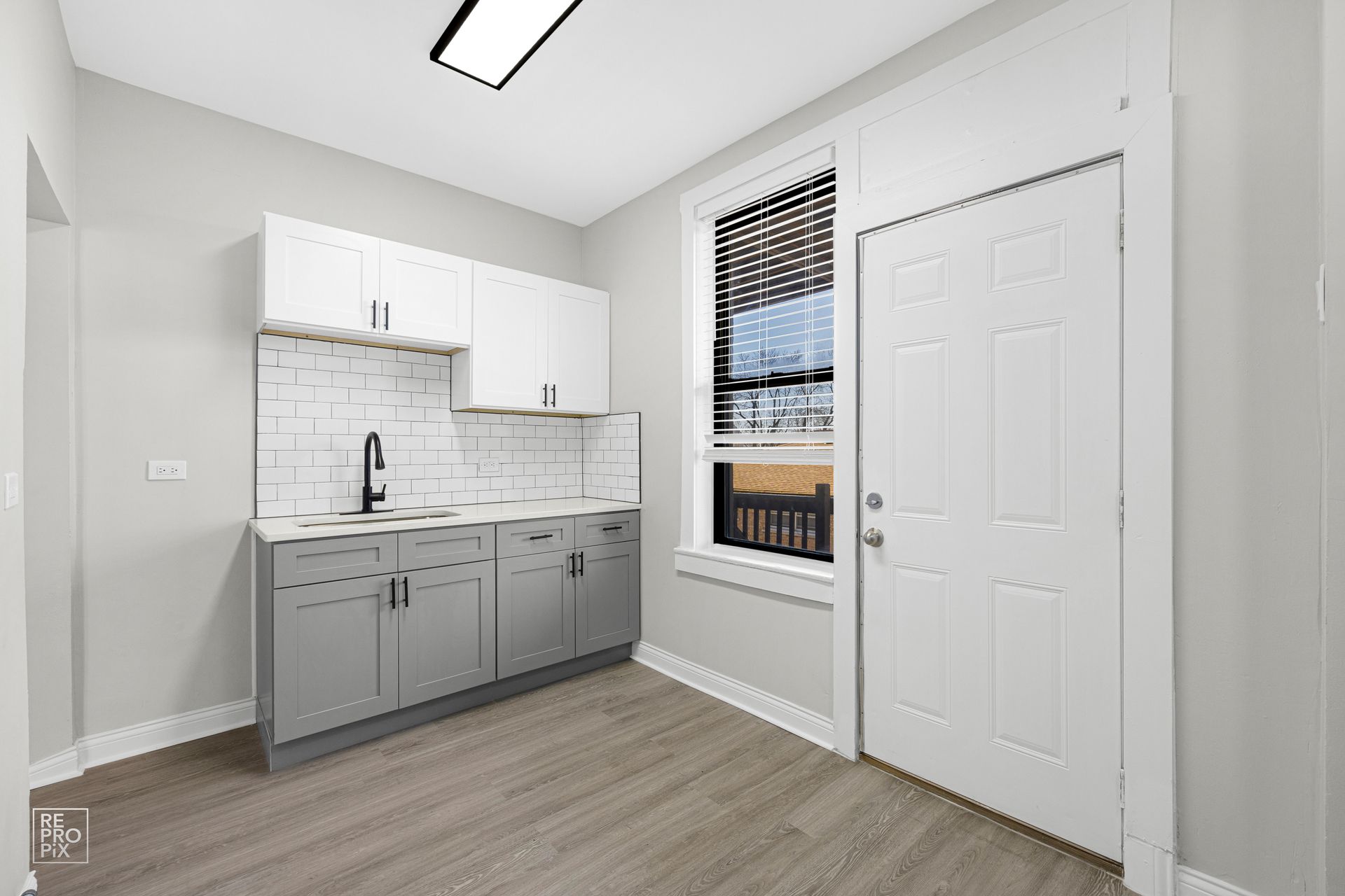 Small kitchen with white and gray cabinets, subway tile backsplash, and window.