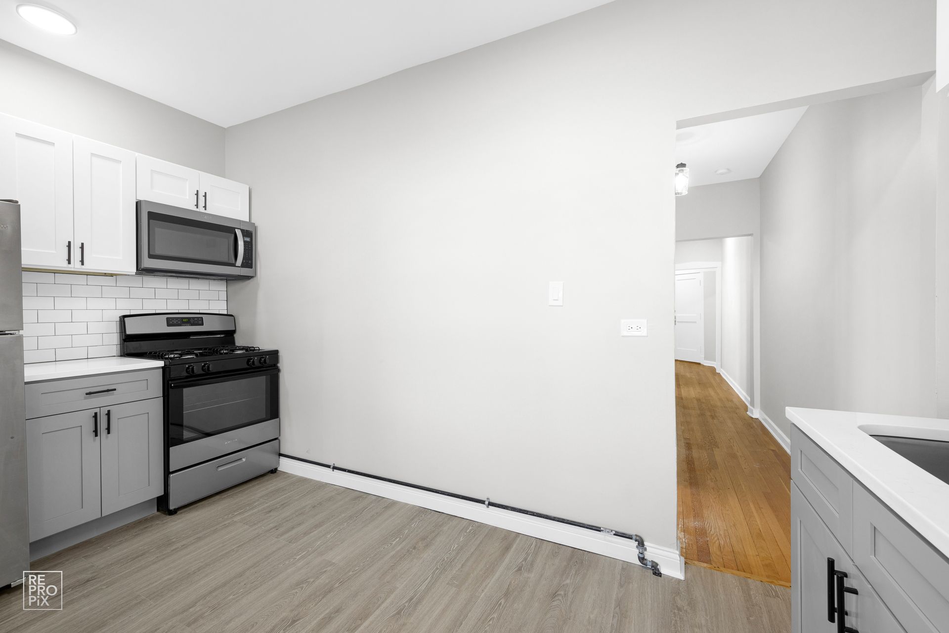 Modern kitchen with gray cabinets, stainless steel appliances, and wood floors.