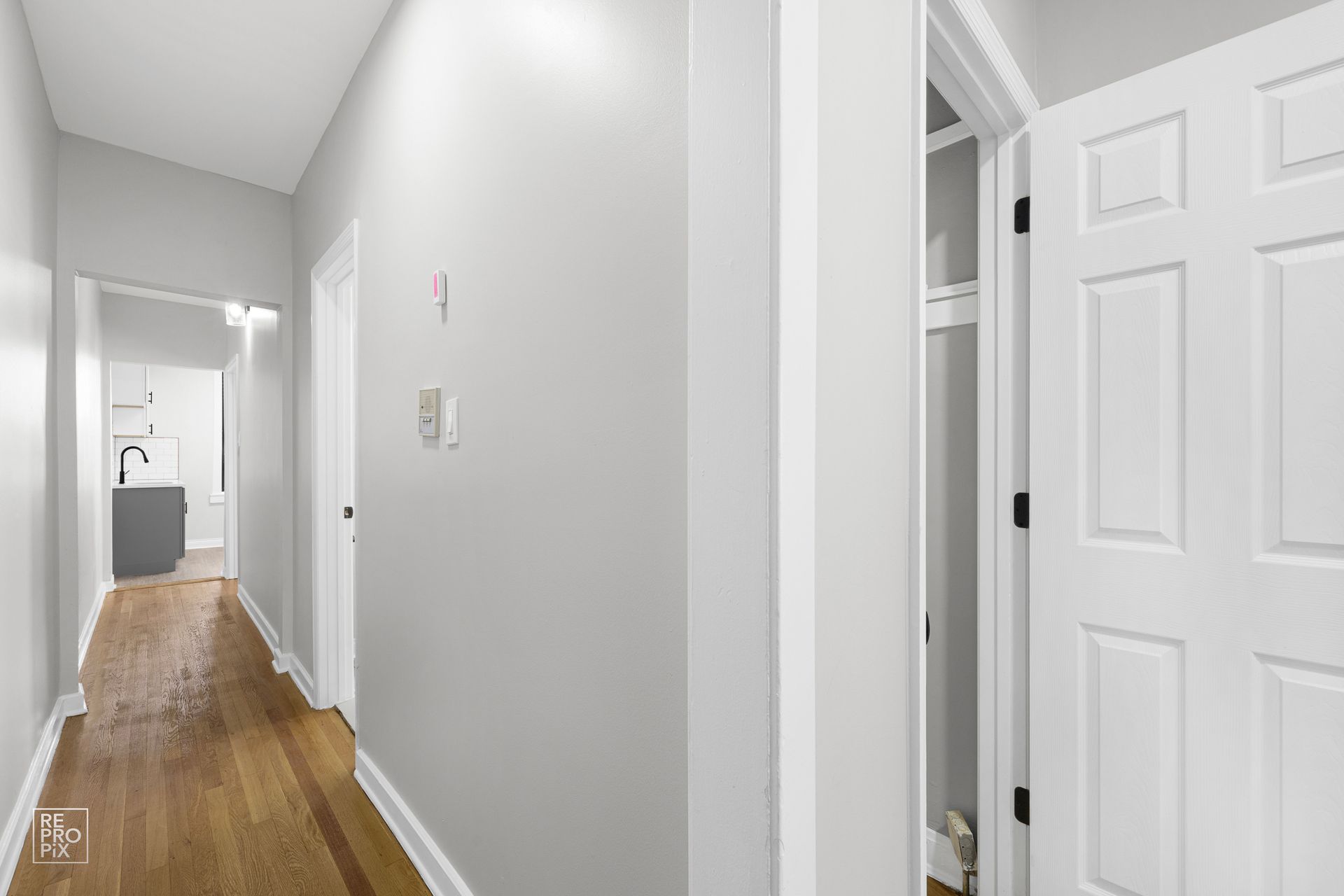 Hallway with light gray walls, wood floor, and open white door to a closet.