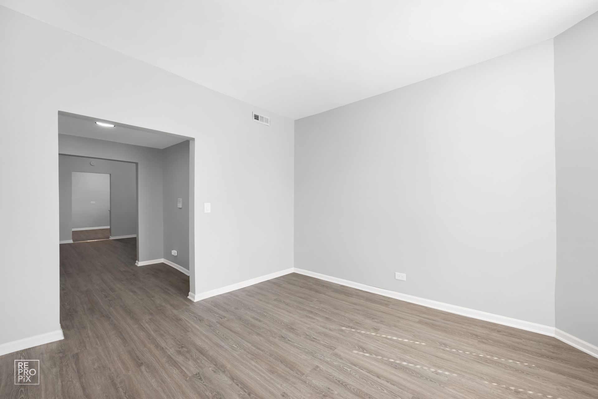 Empty room with gray walls and wood-look flooring. An open doorway leads to a hallway.