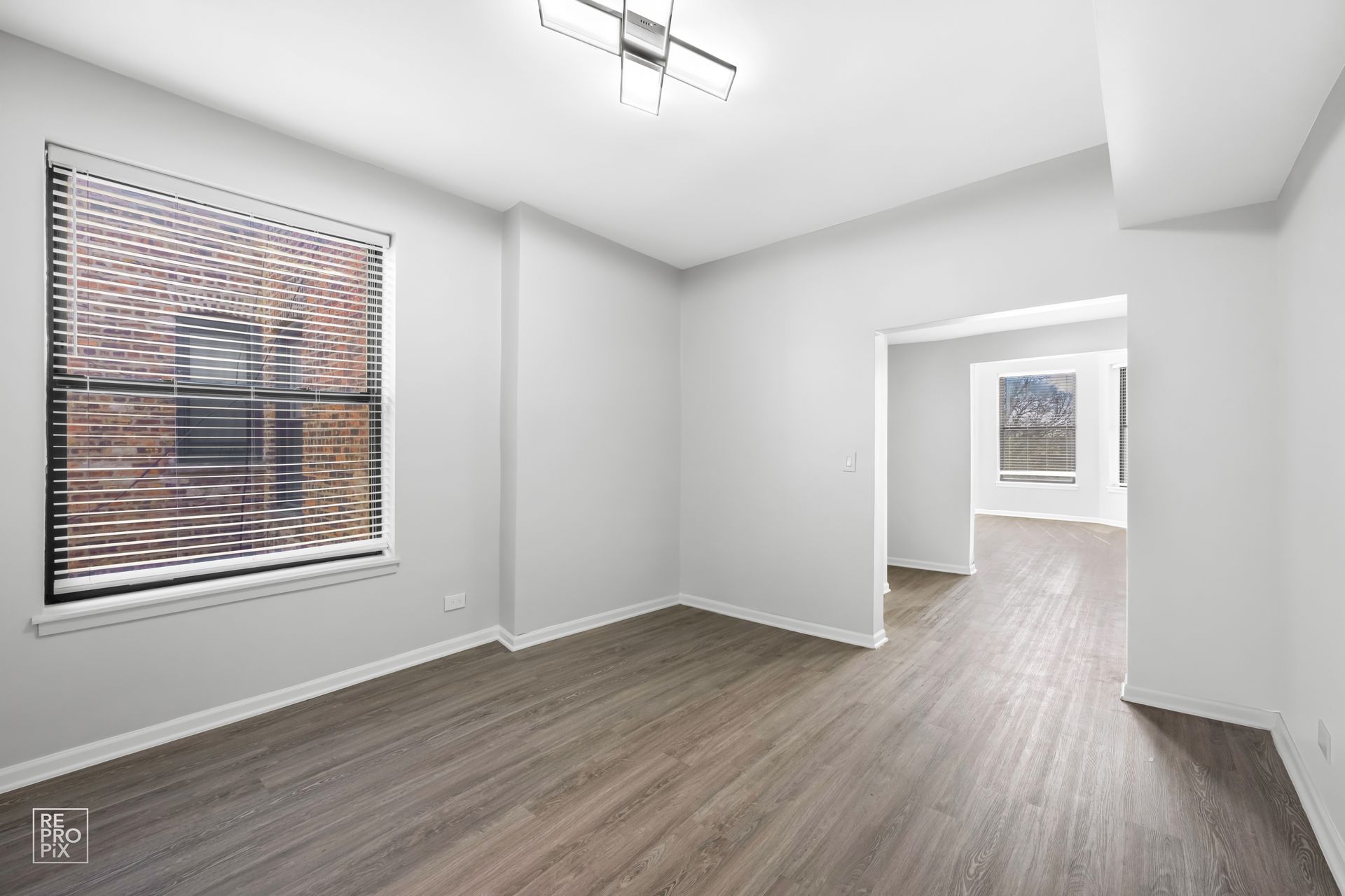 Empty room with gray walls, wood-look flooring, and a large window with blinds.