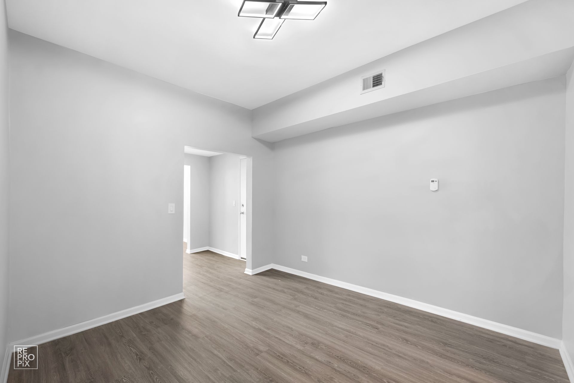 Empty room with gray walls and wood-look floor. Ceiling light. Doorway visible.