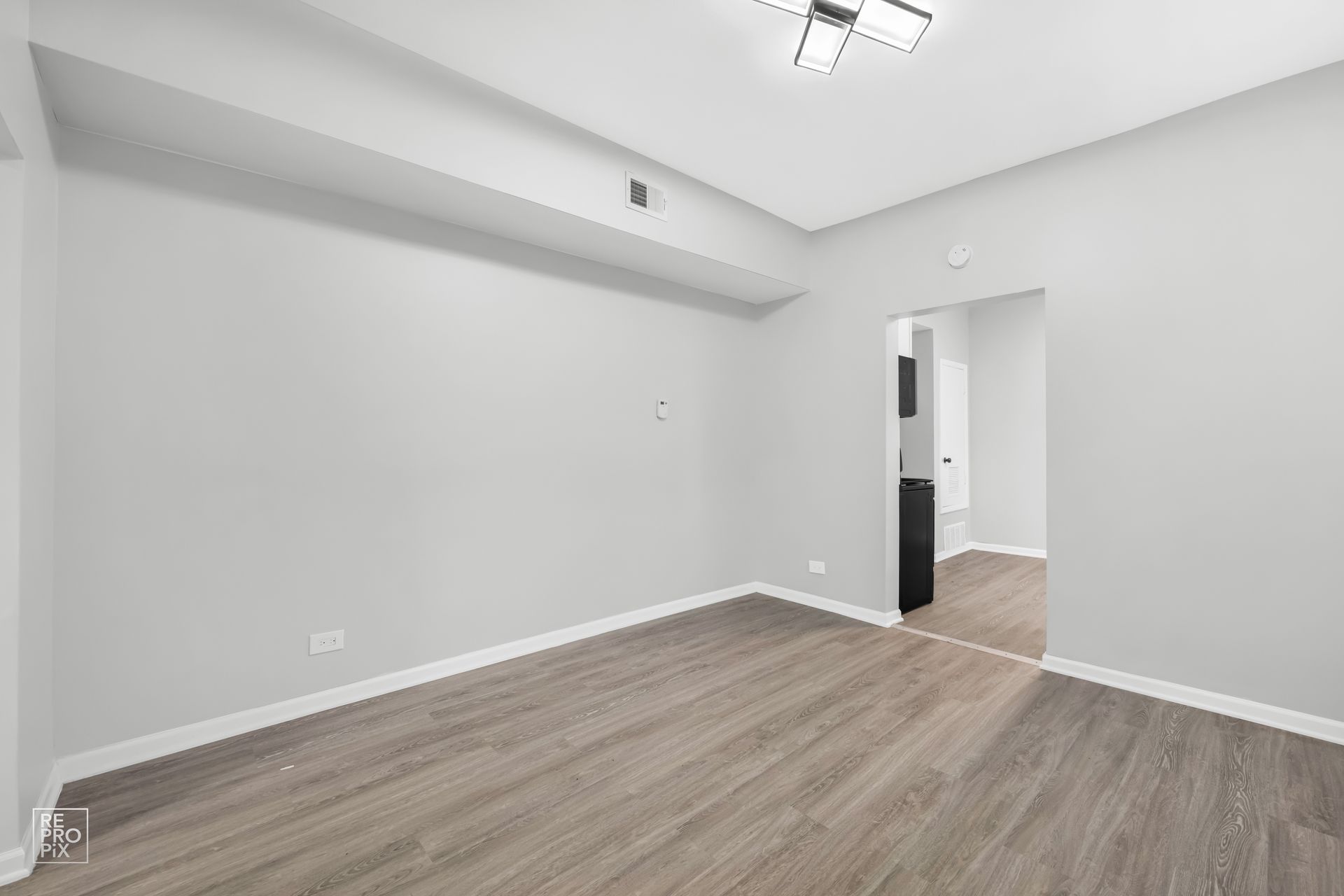 Empty room with gray walls, wood flooring, and a doorway.