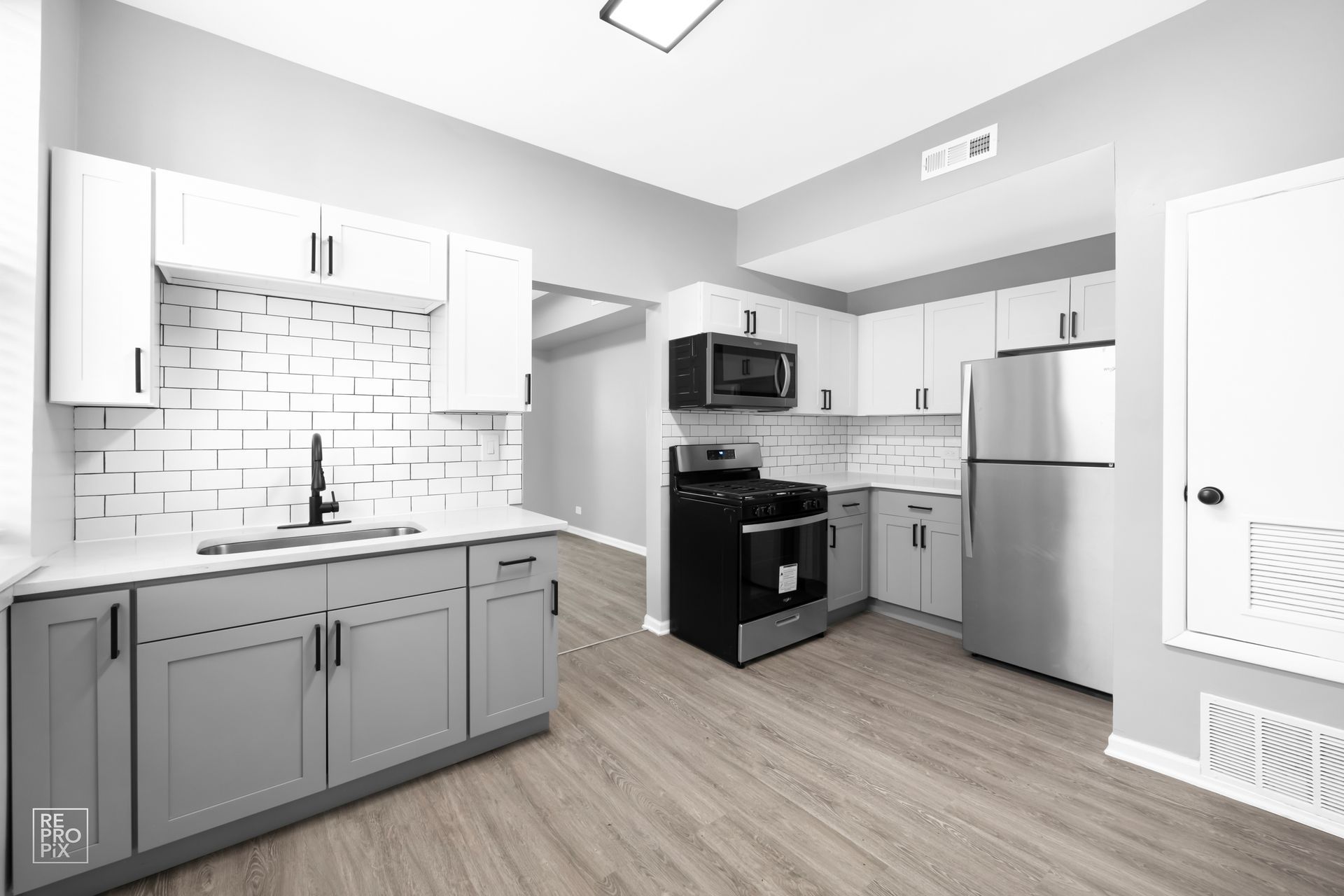 Gray and white kitchen with stainless steel appliances and wood-look flooring.