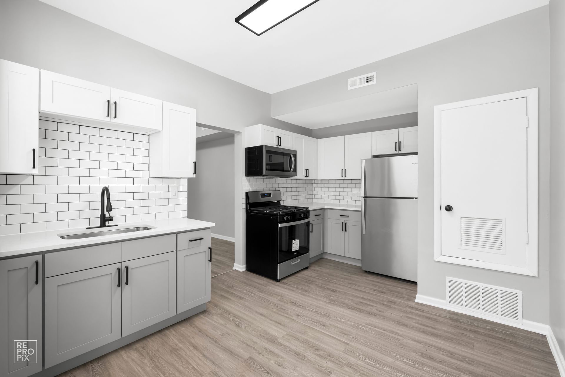 Kitchen with gray and white cabinets, stainless steel appliances, and wood-look flooring.