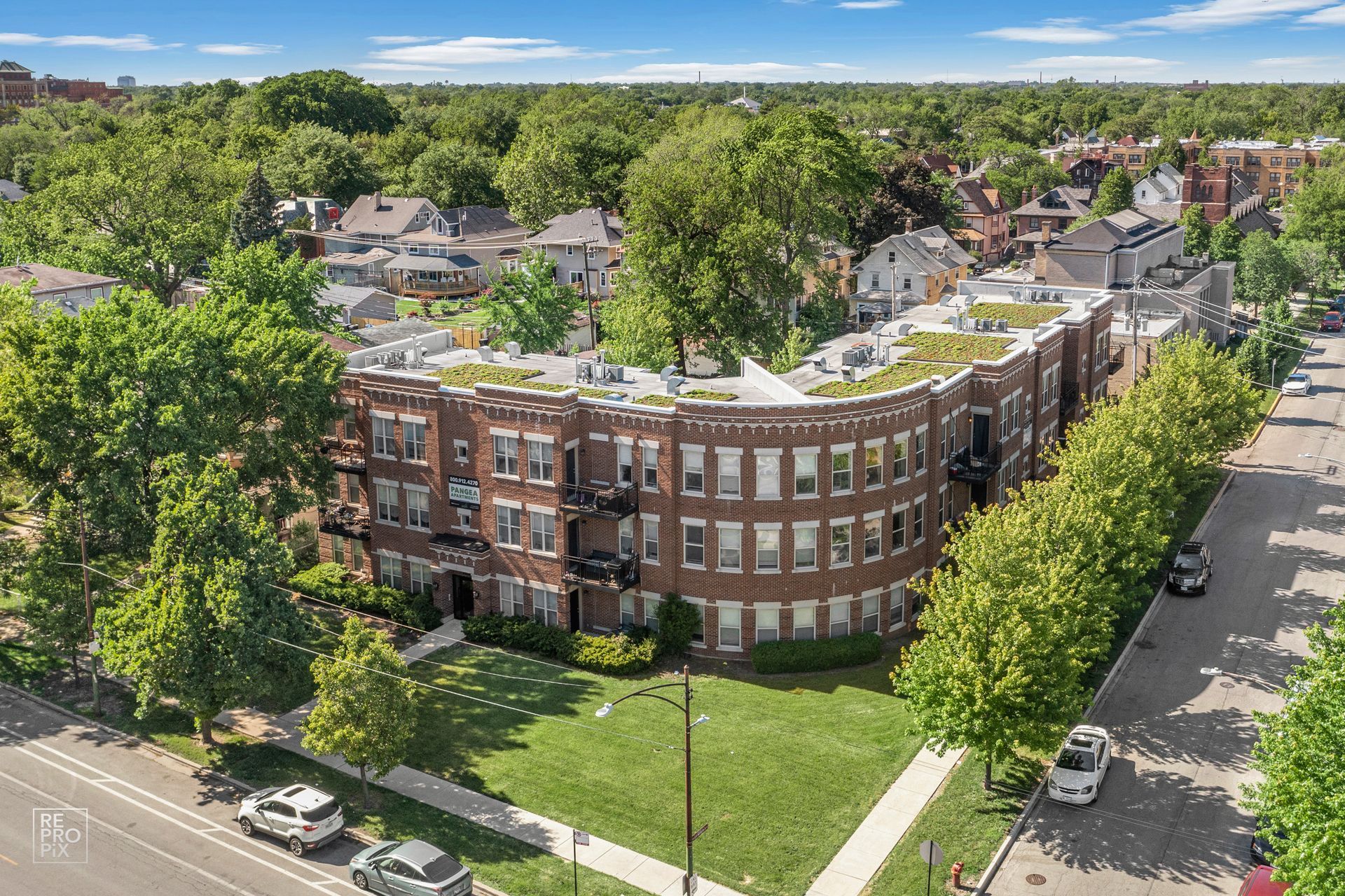 Brick apartment building with green roof, trees, and street.