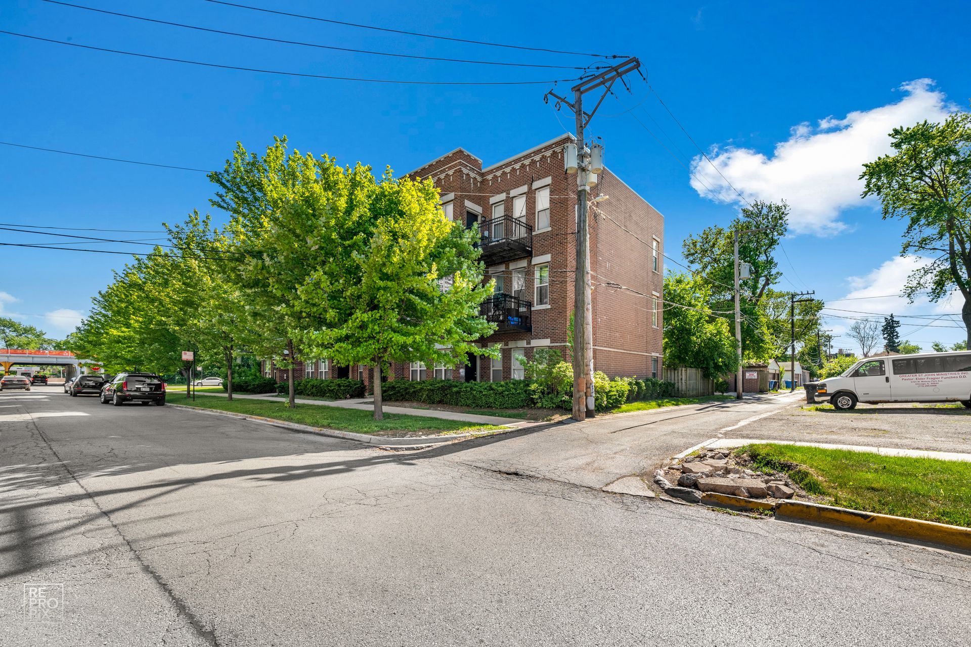 Brick apartment building on a street corner, with trees and cars on a sunny day.