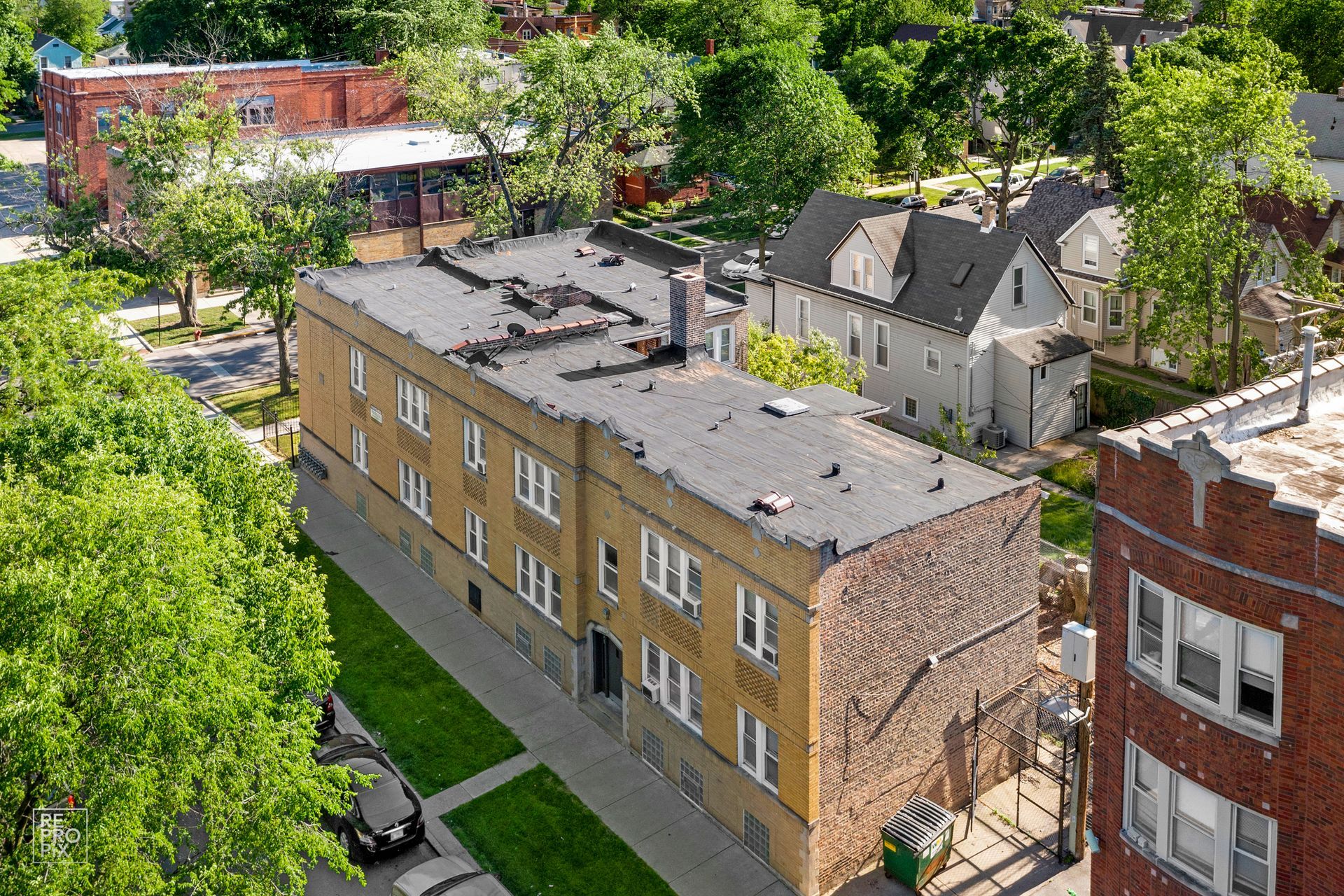 Aerial view of a three-story apartment building with a flat roof and surrounding trees.