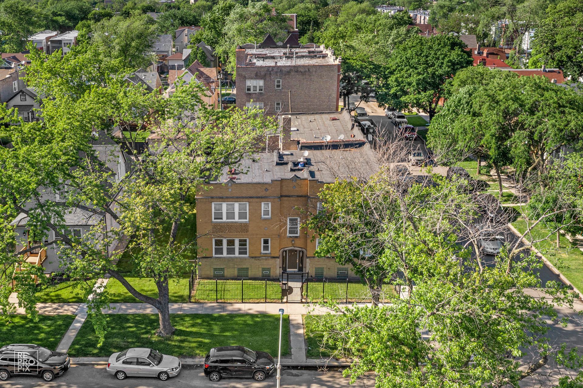 An aerial view of a tan brick building surrounded by trees and residential homes. Cars parked on the street.
