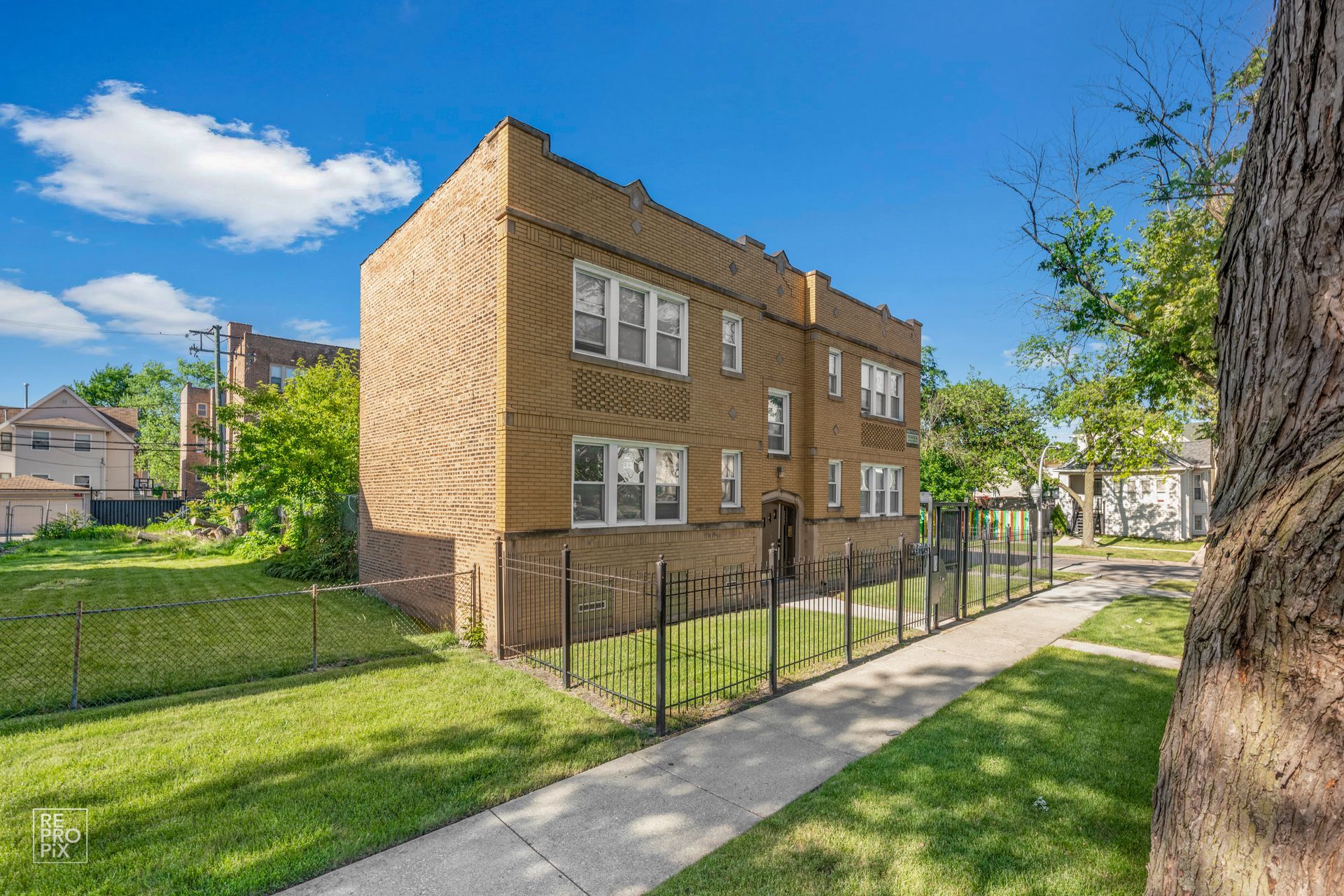 Two-story brick building with multiple windows, next to a sidewalk and green lawn under a blue sky.
