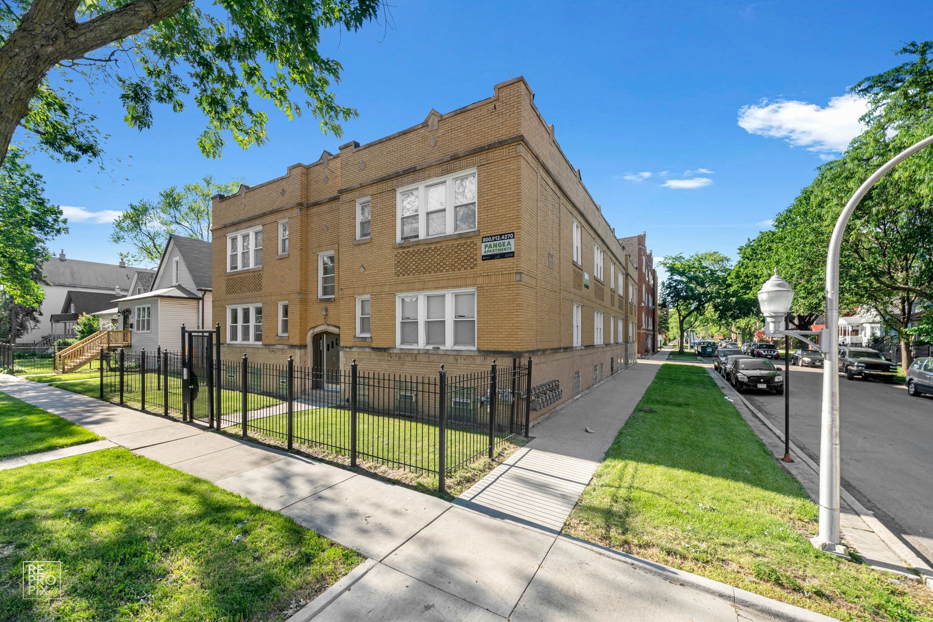 Brick apartment building with black fence, trees, and street.