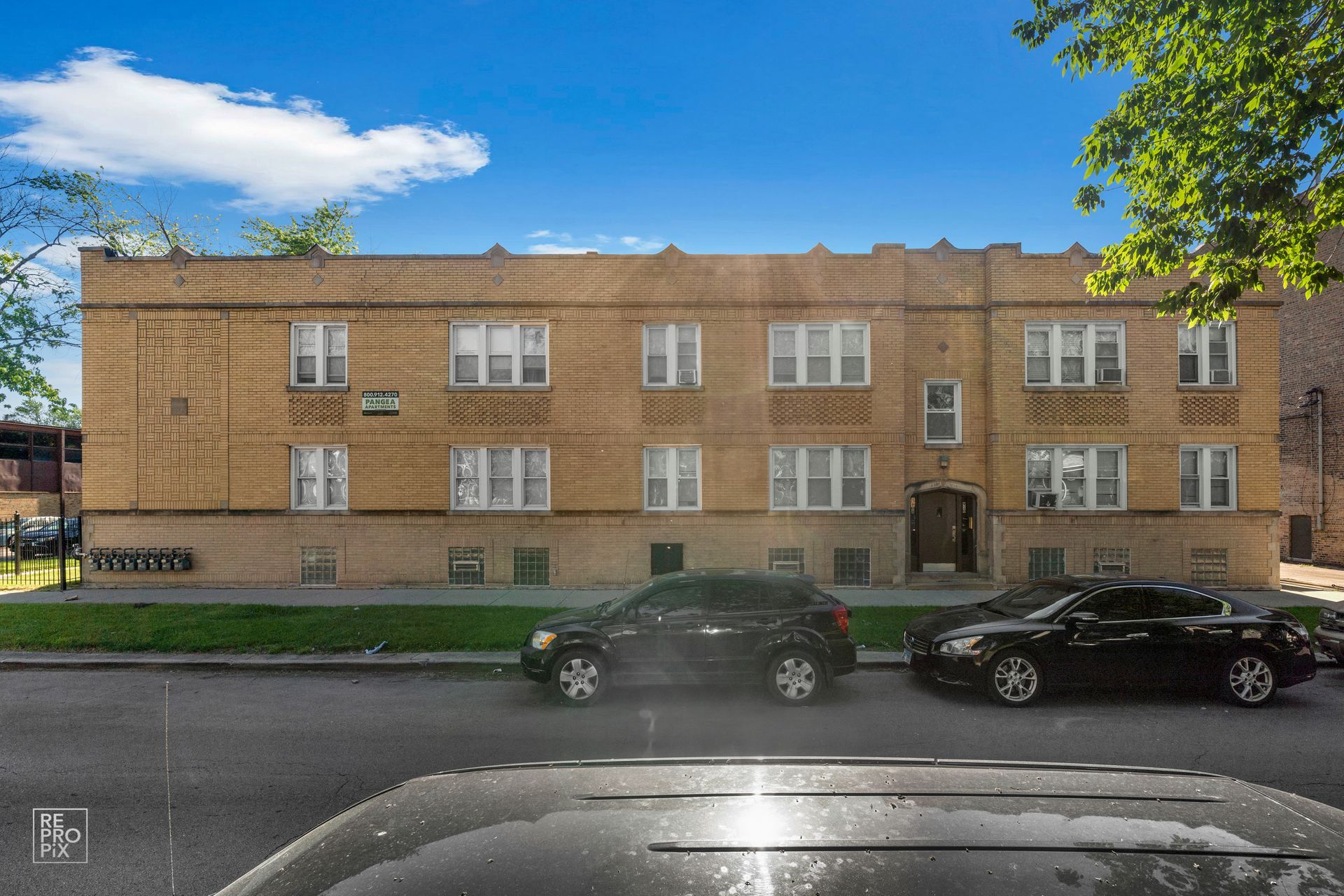 Two-story brick apartment building with parked cars on a sunny street.