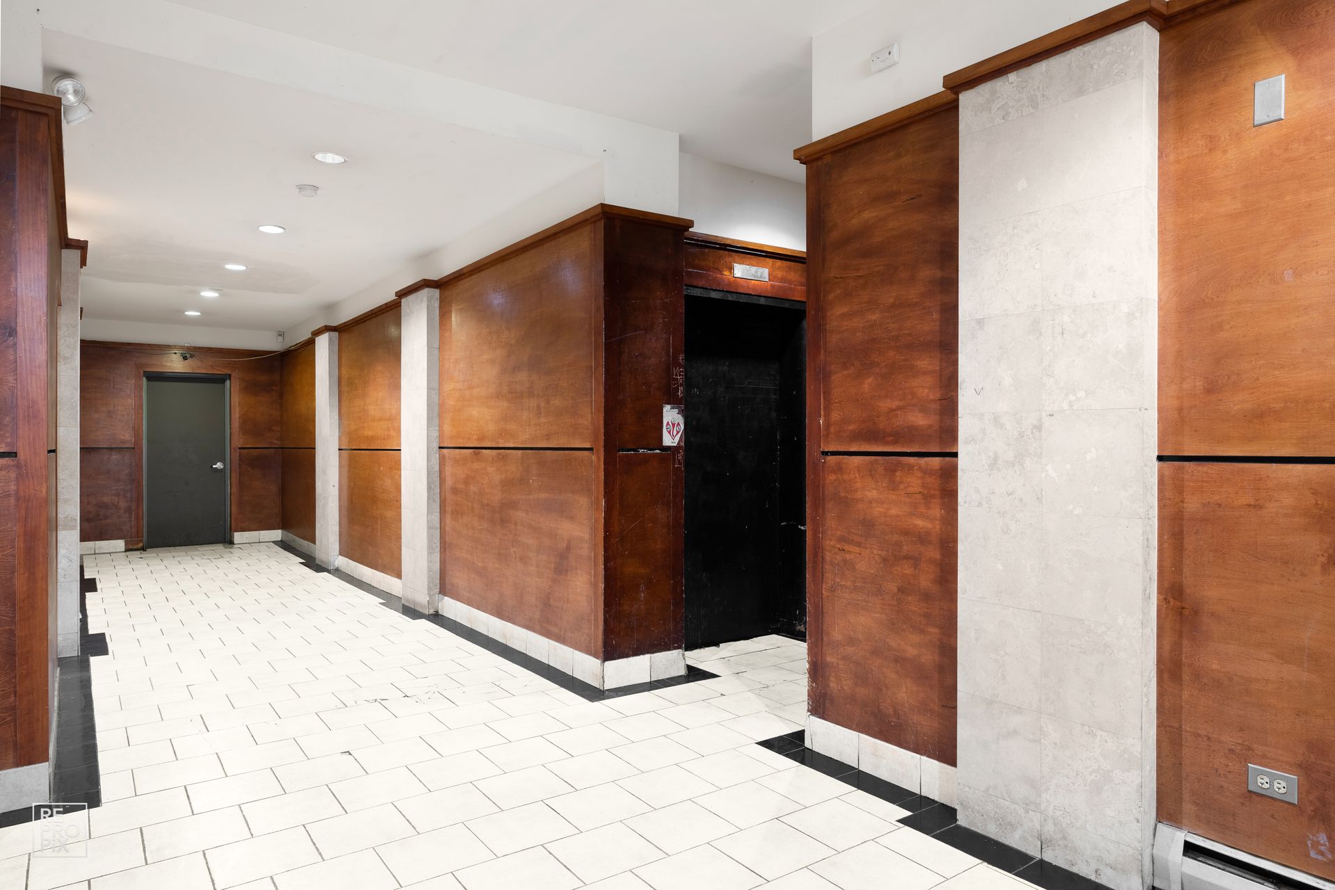 Hallway with wood paneling, white tiles, and black elevator door.