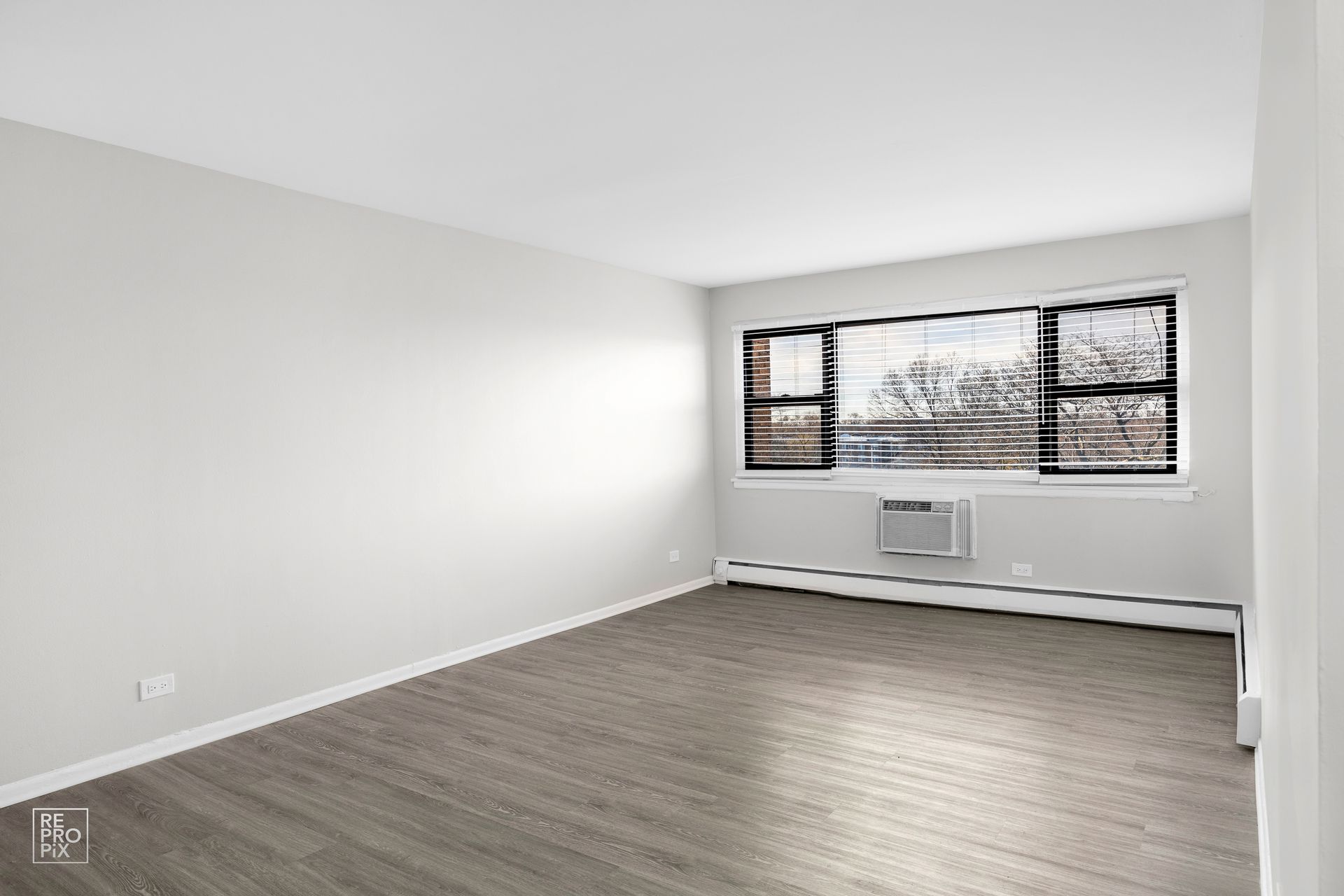 Empty room with a large window, light gray walls, and gray flooring.
