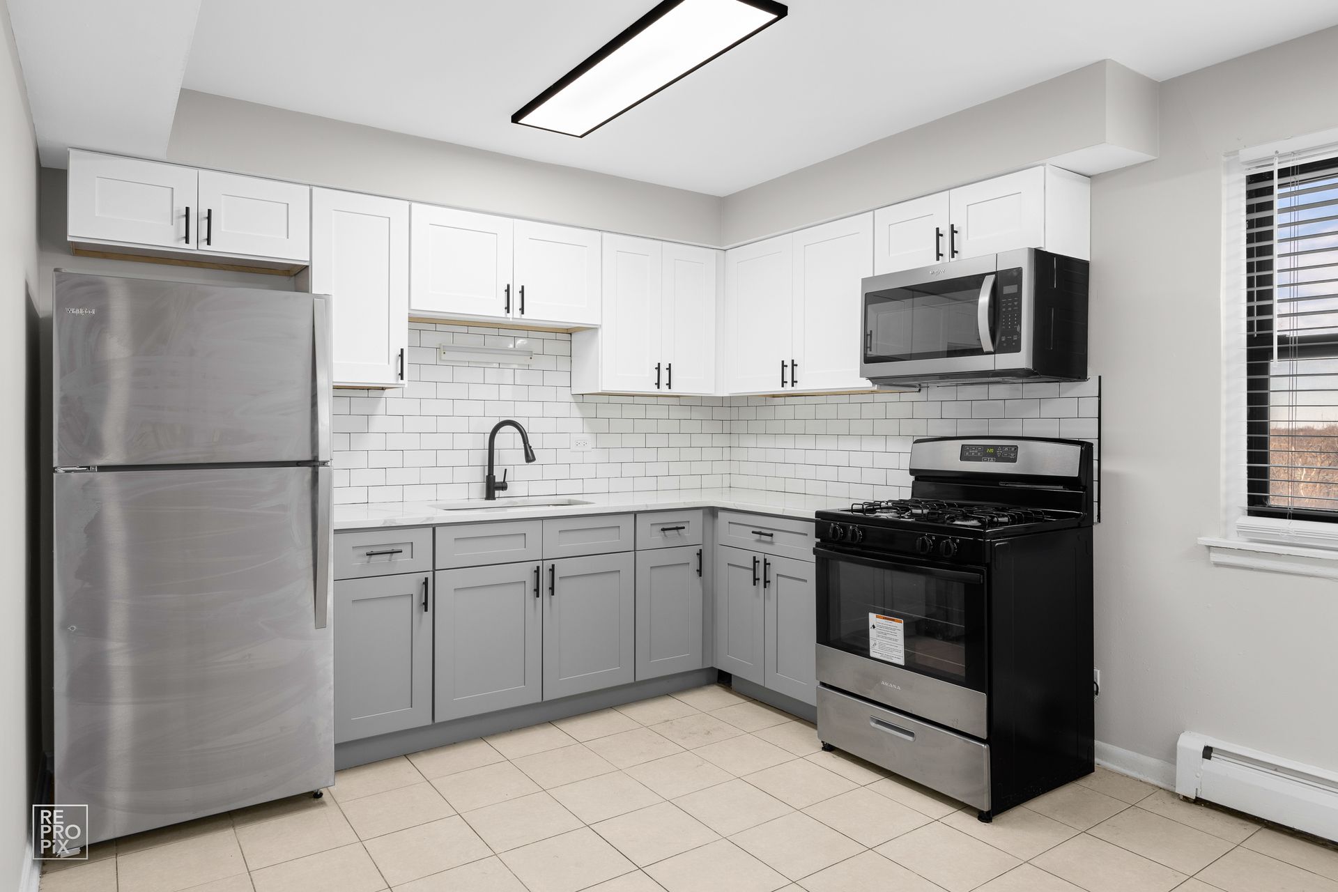 Modern kitchen with gray and white cabinets, stainless steel appliances, and a window.
