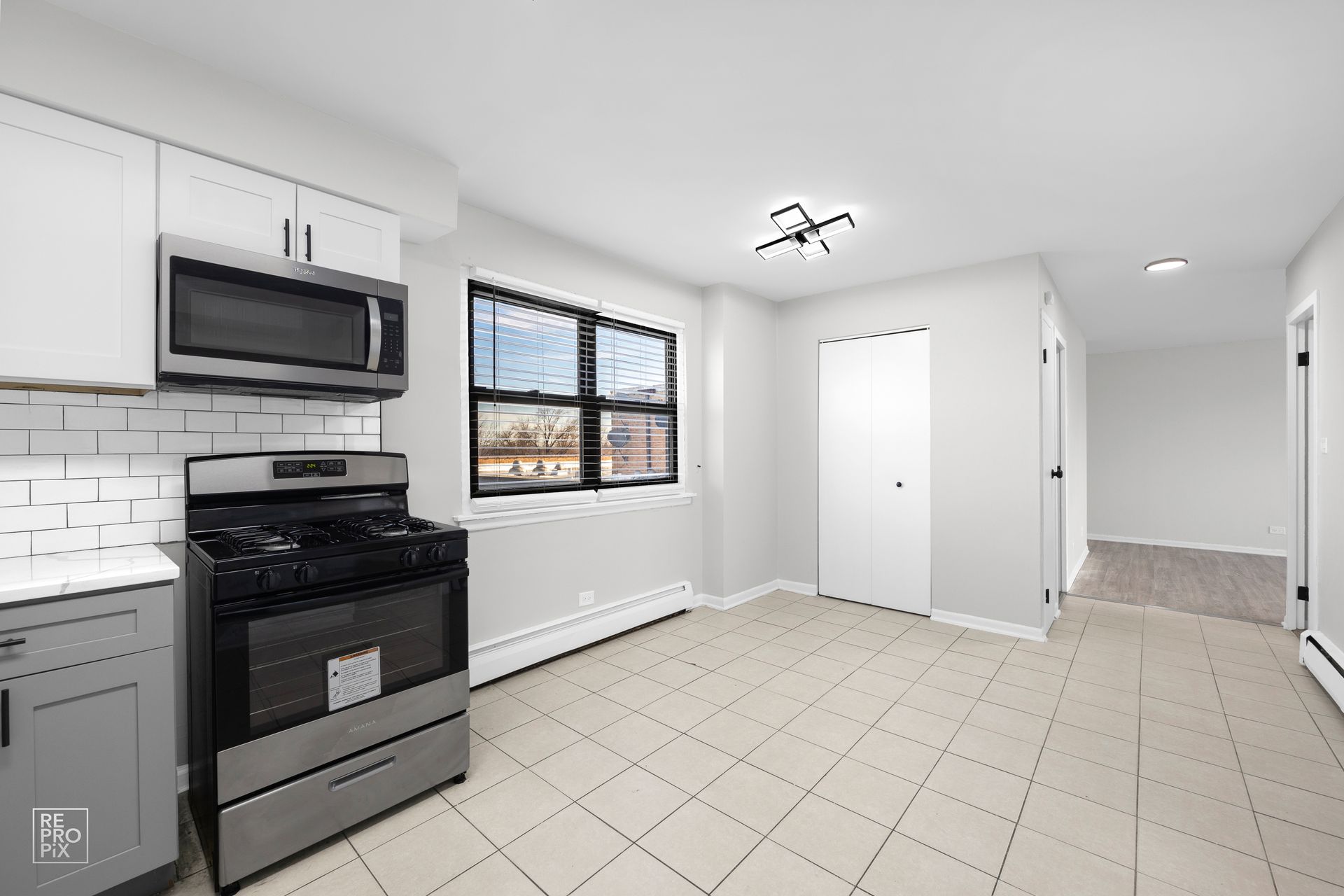 Kitchen with stainless steel appliances, gray cabinets, white tile backsplash, and light gray walls.